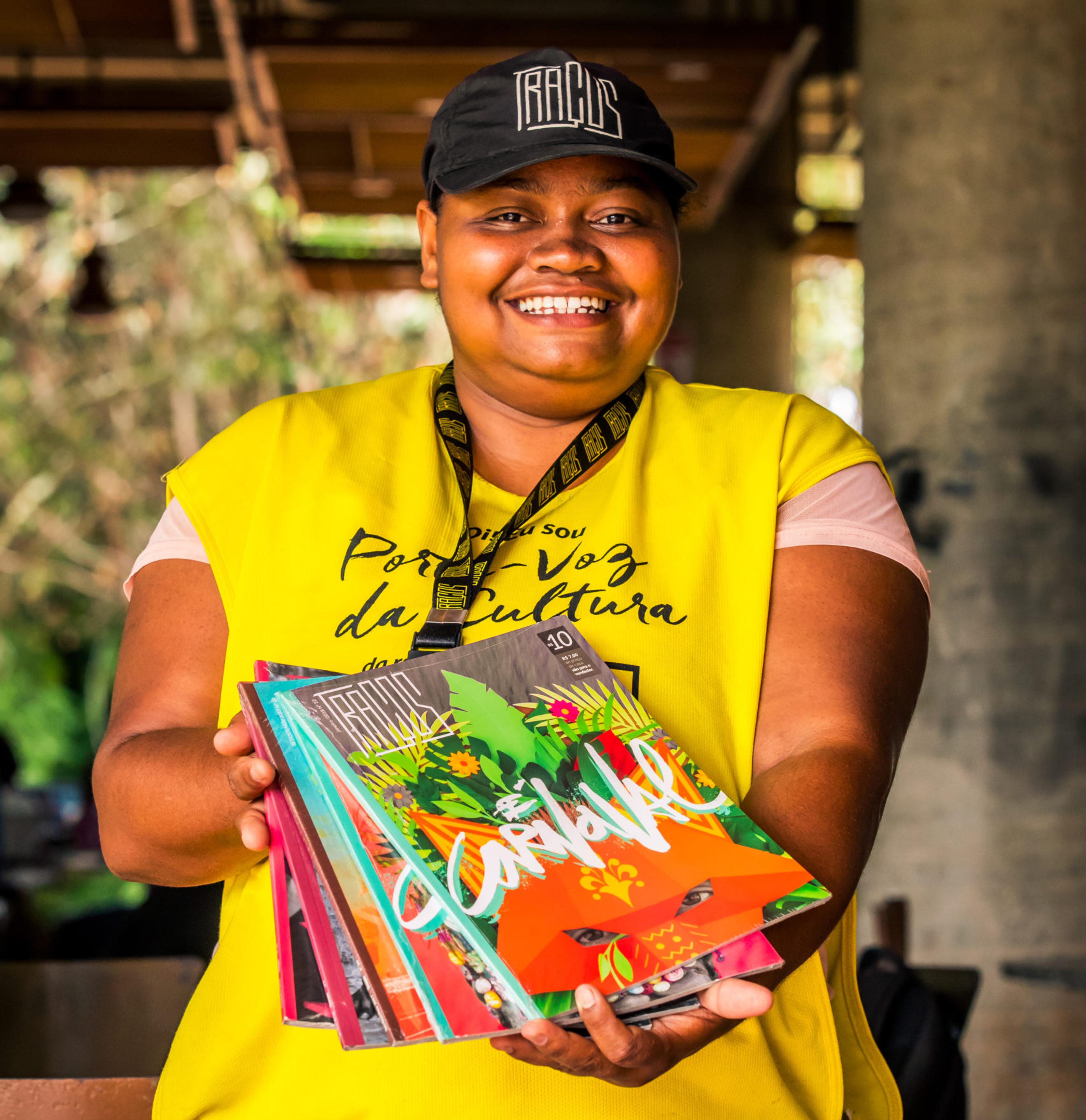 Woman with yellow vest holding Tracos street paper magazine