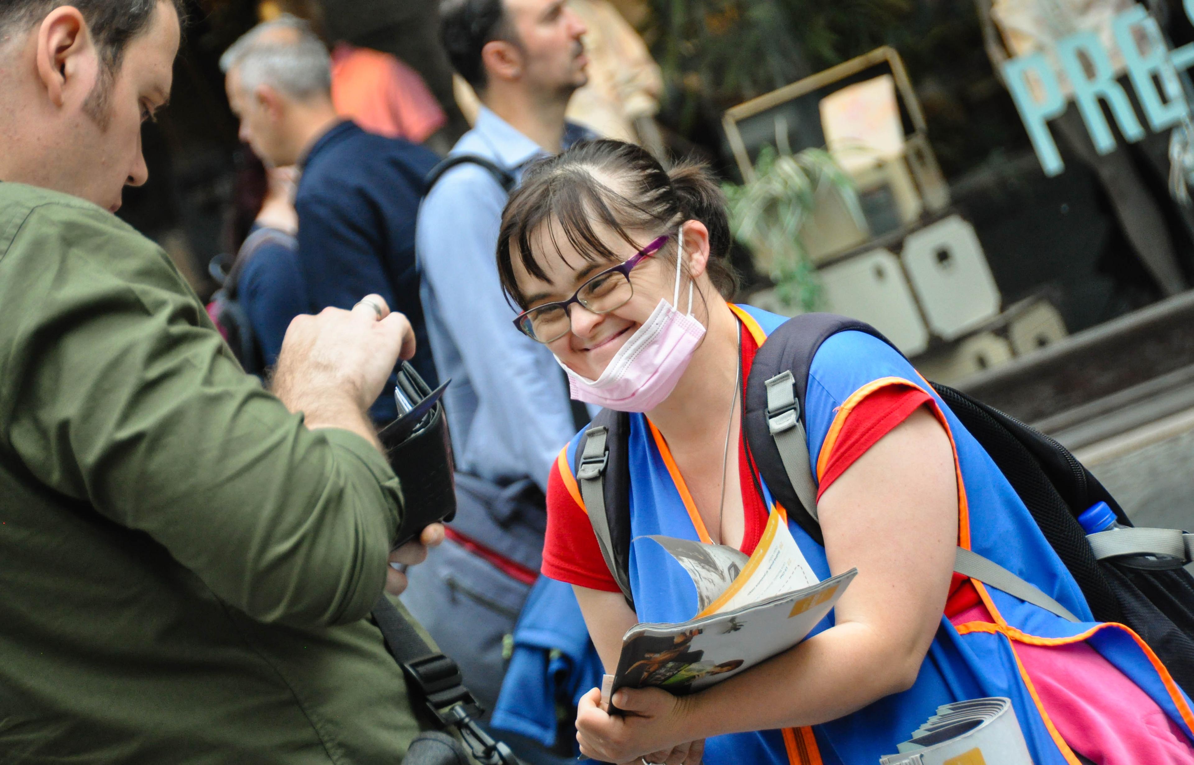 Woman wearing a blue vest and handing out Liceulice street paper in Serbia