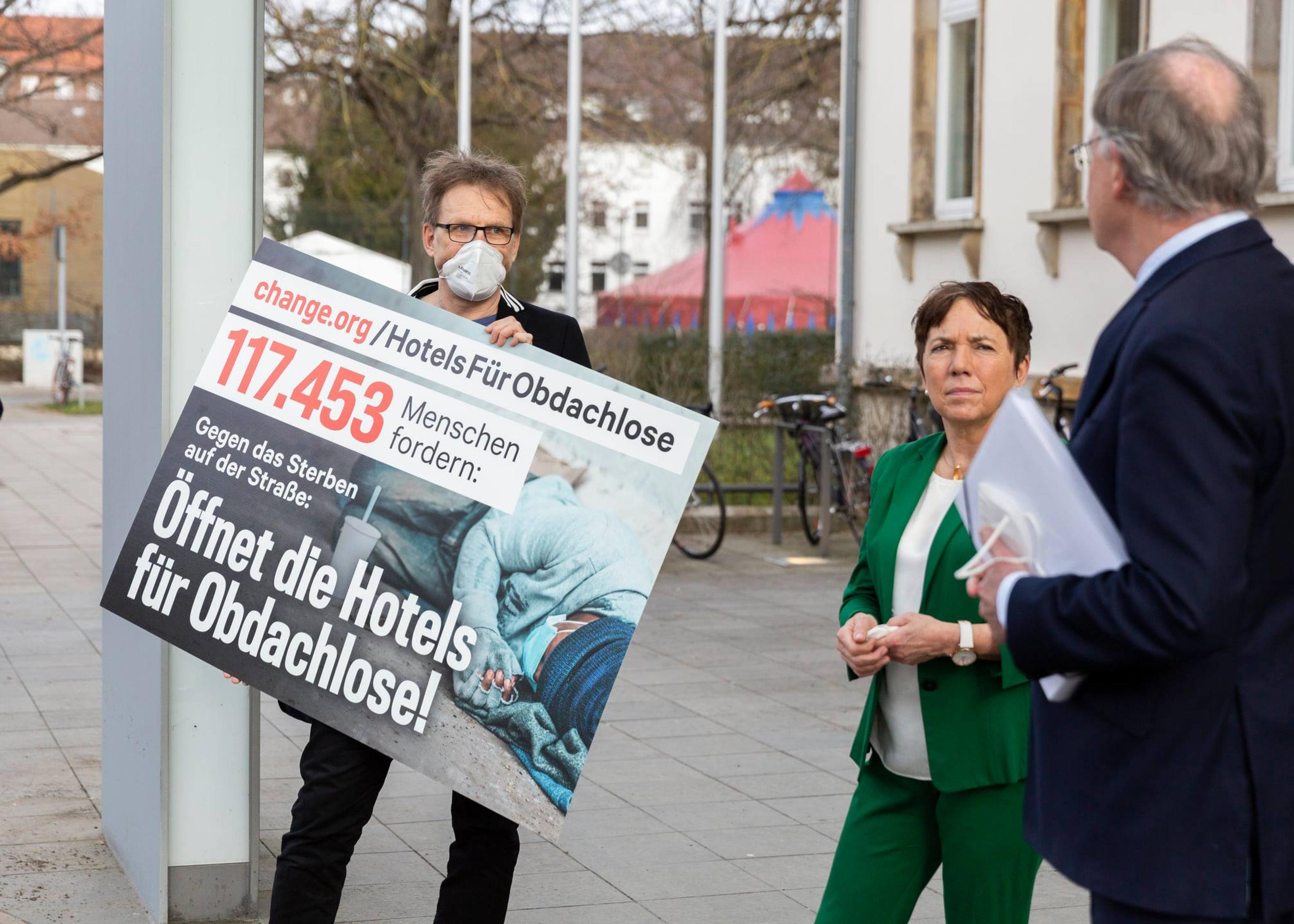 A man in a mask holds a sign detailing a petition to get the homeless community indoors during the height of the Covid-19 pandemic