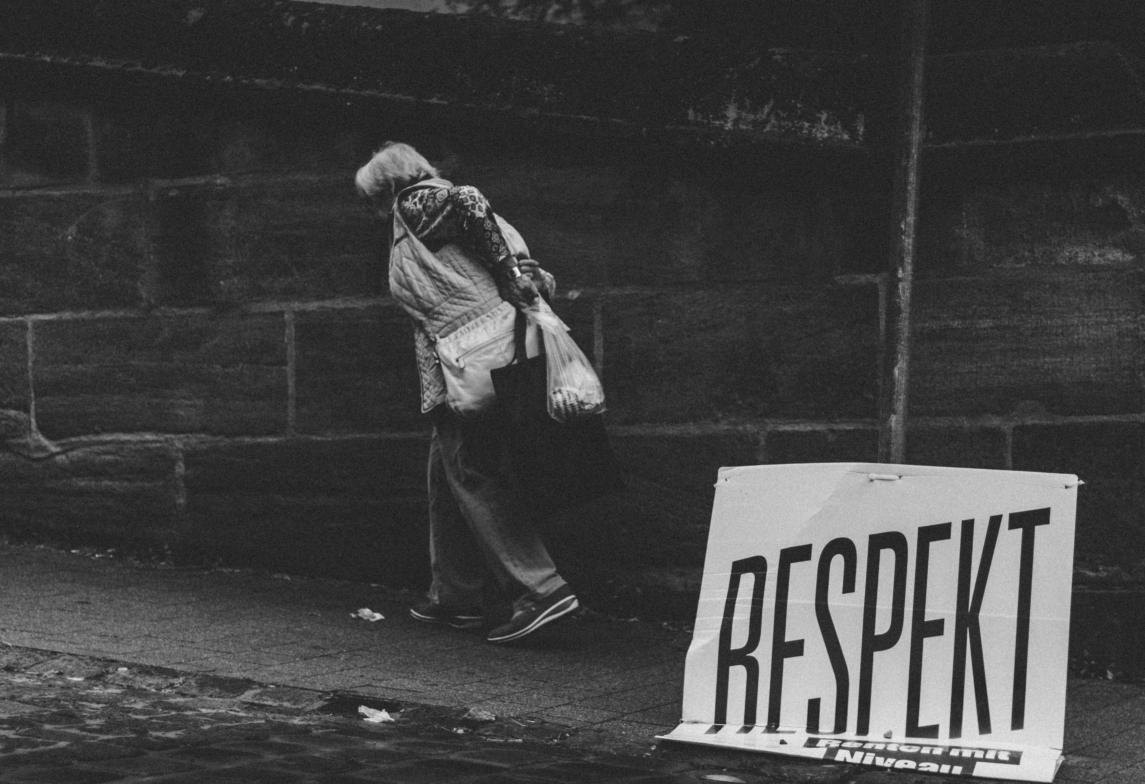 black and white photo of a woman walking down a street, past a sign that says 'respekt'