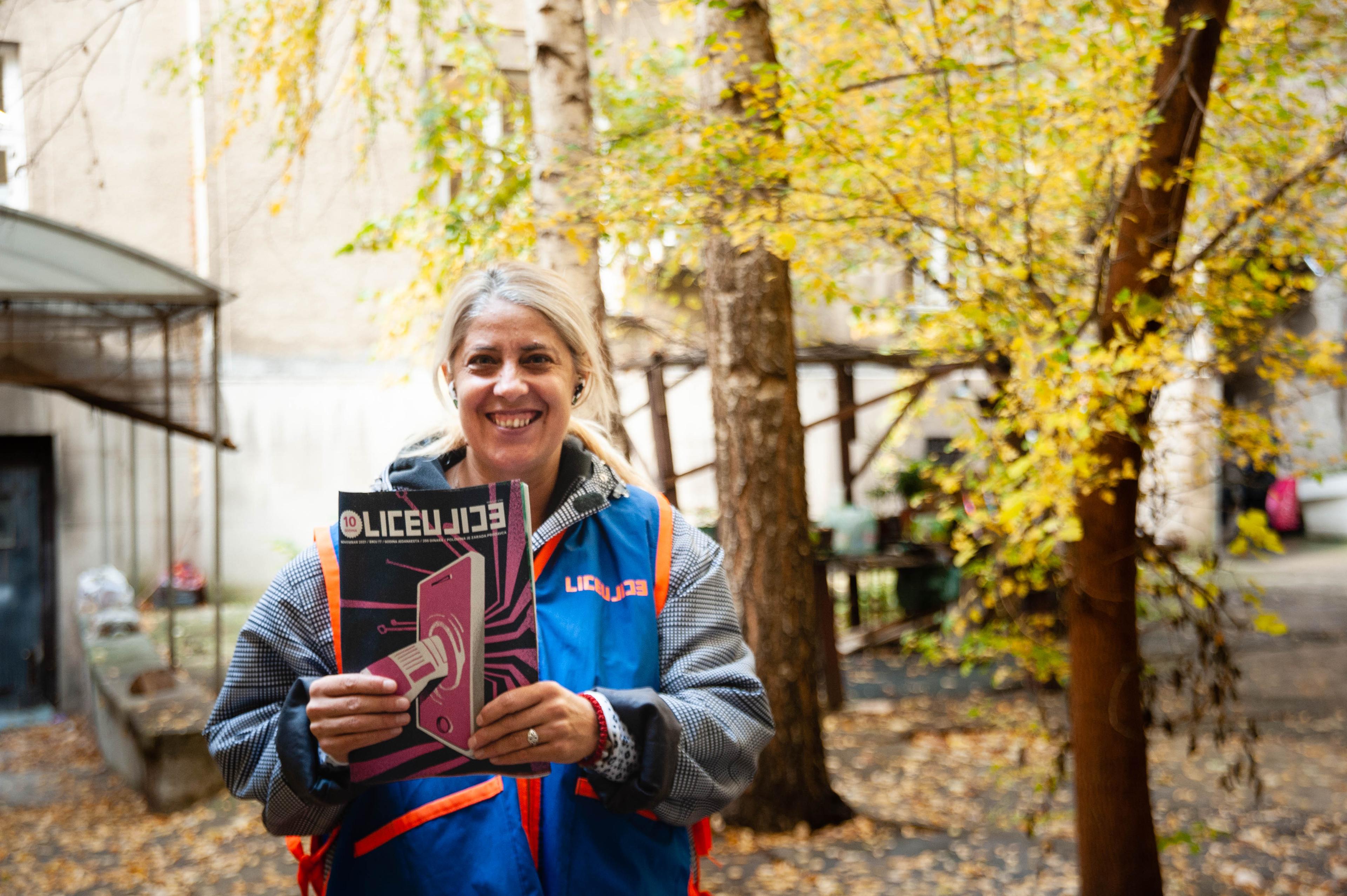 A woman holds a magazine under a tree