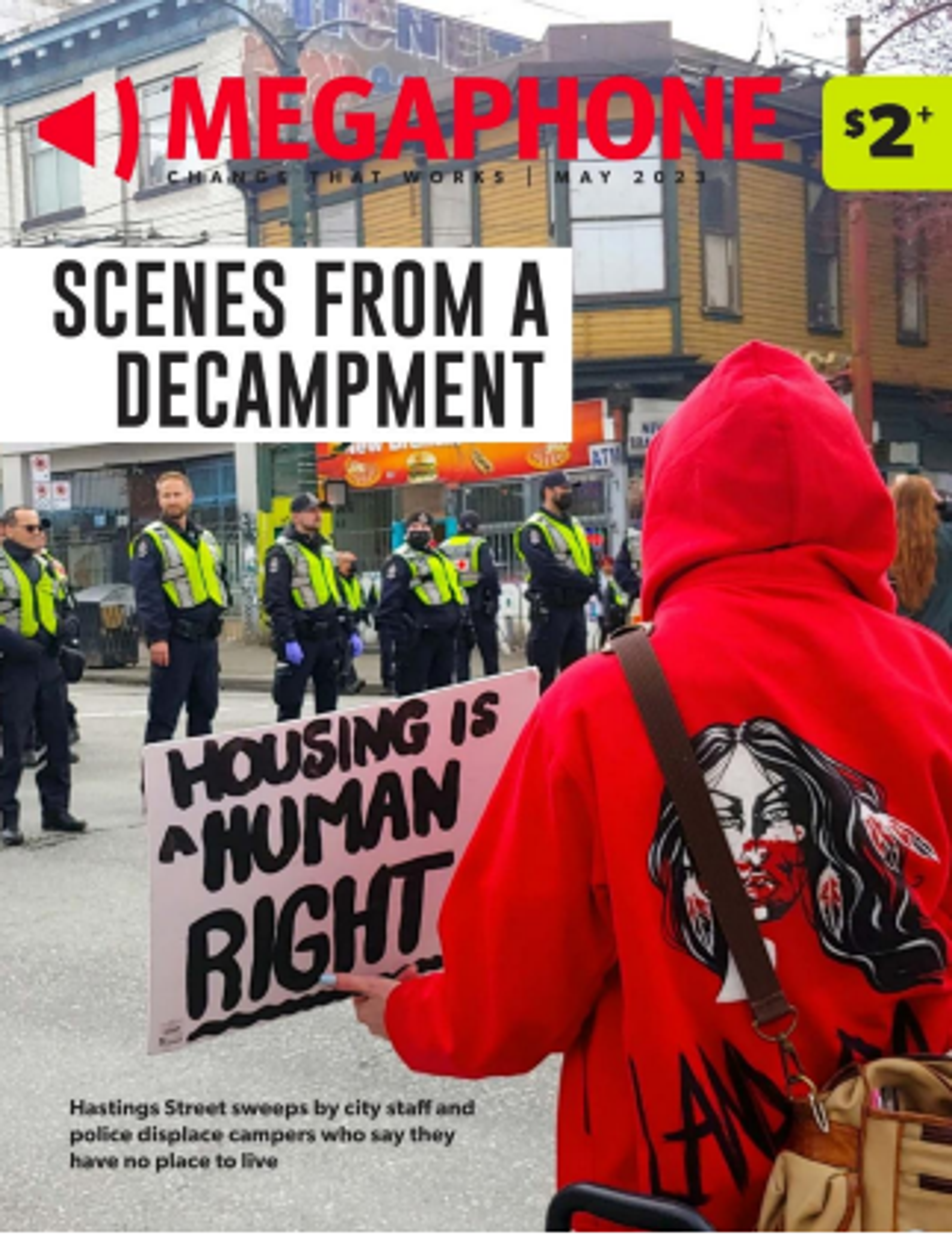 man in red hoodie facing police, holding a placard reading 'housing is a human right'