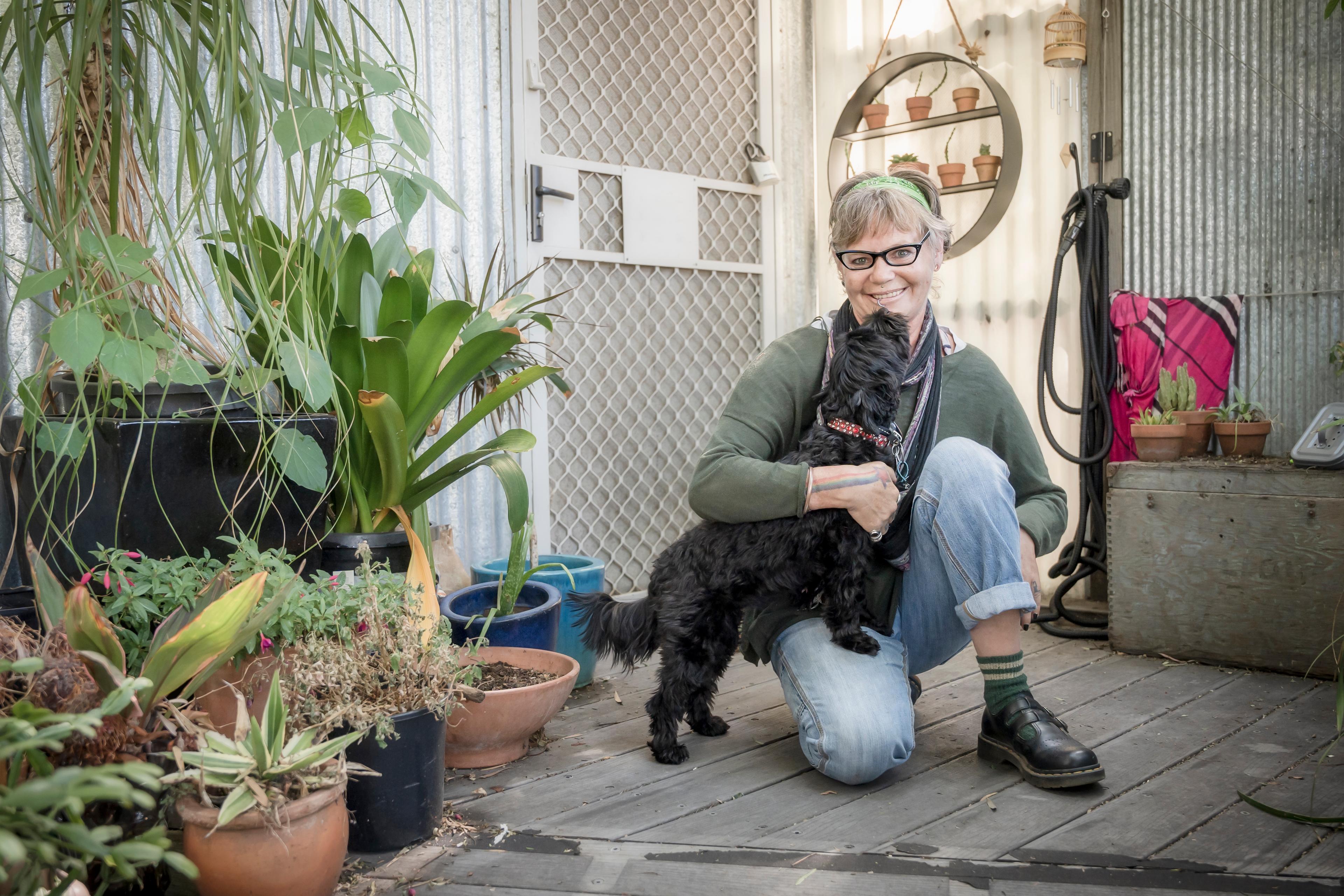 Danni kneels on the floor with her dog that has black fur.