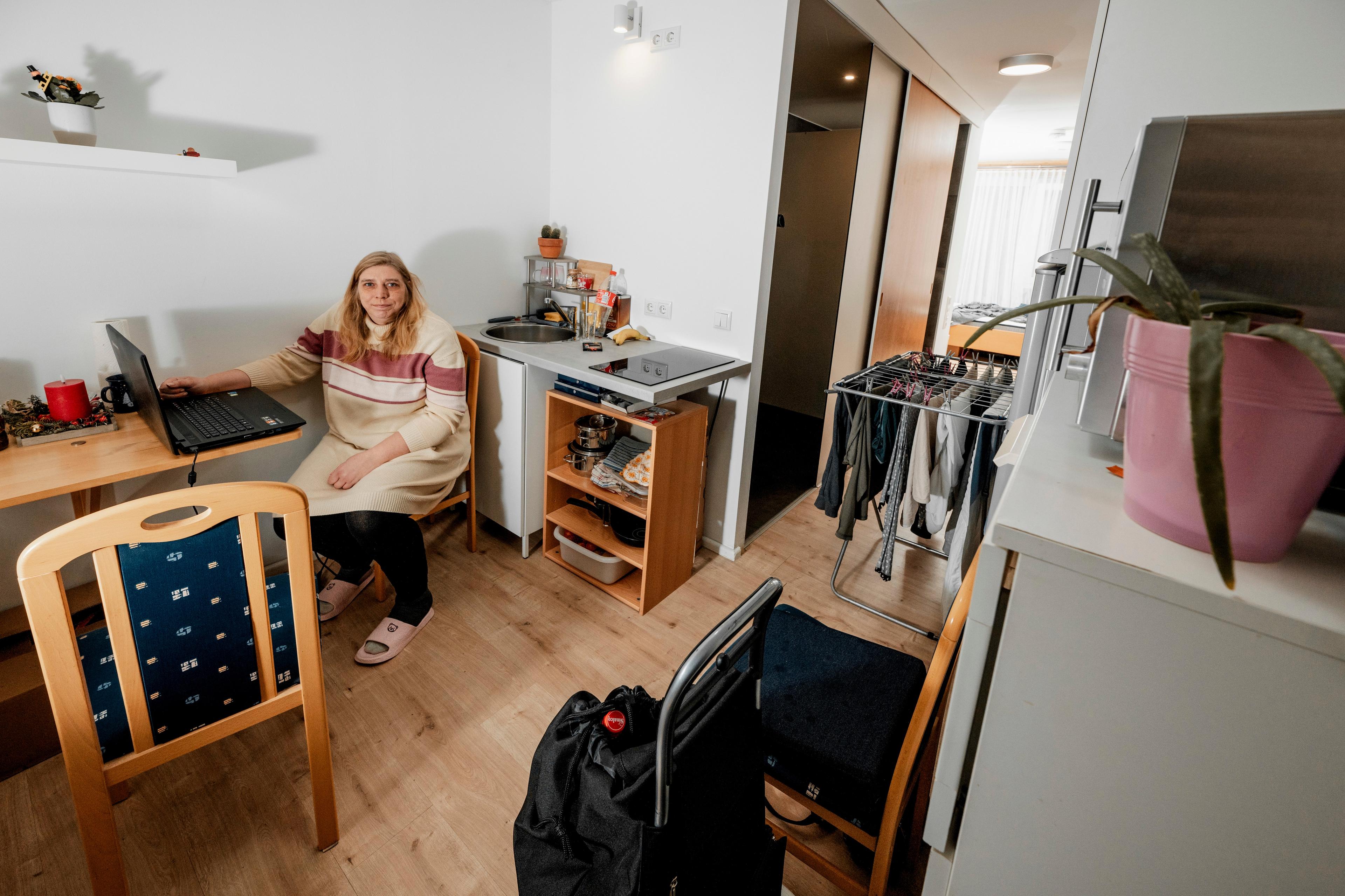 a woman sits at a kitchen table inside a small apartment