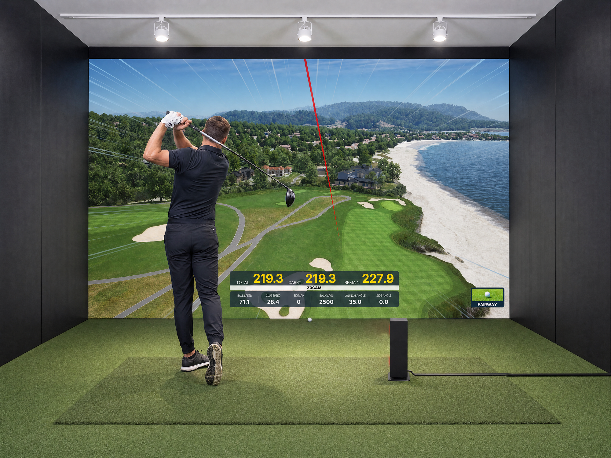 A man swings a golf club in a Uneekor indoor golf simulator, with a large screen displaying a virtual golf course by a beach and golf data.
