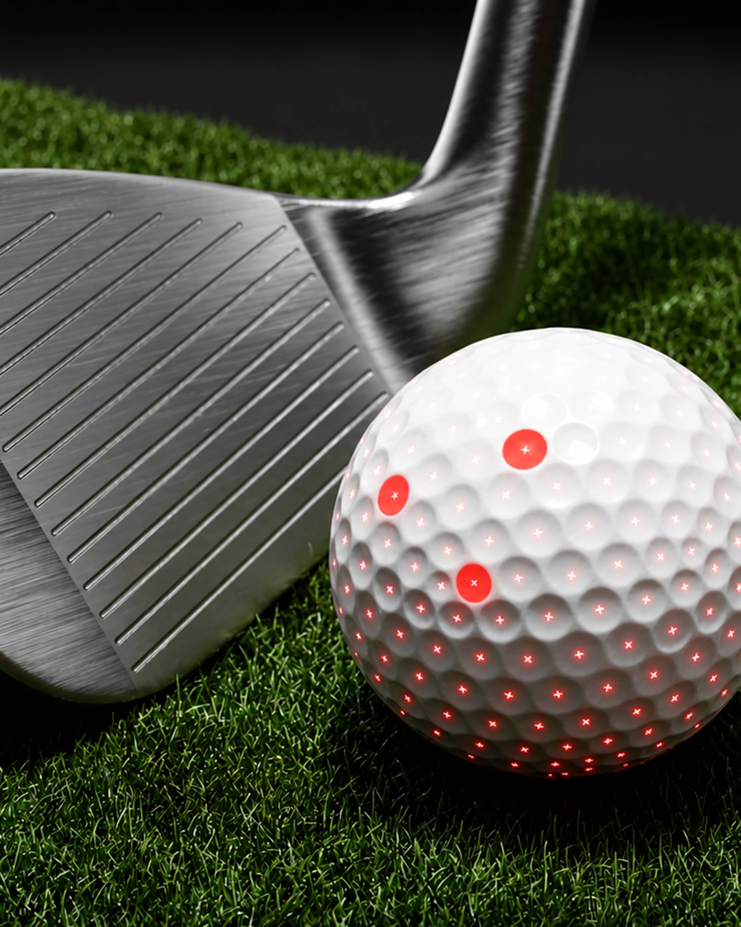 White golf ball with red glowing lights next to a golf club on green grass.