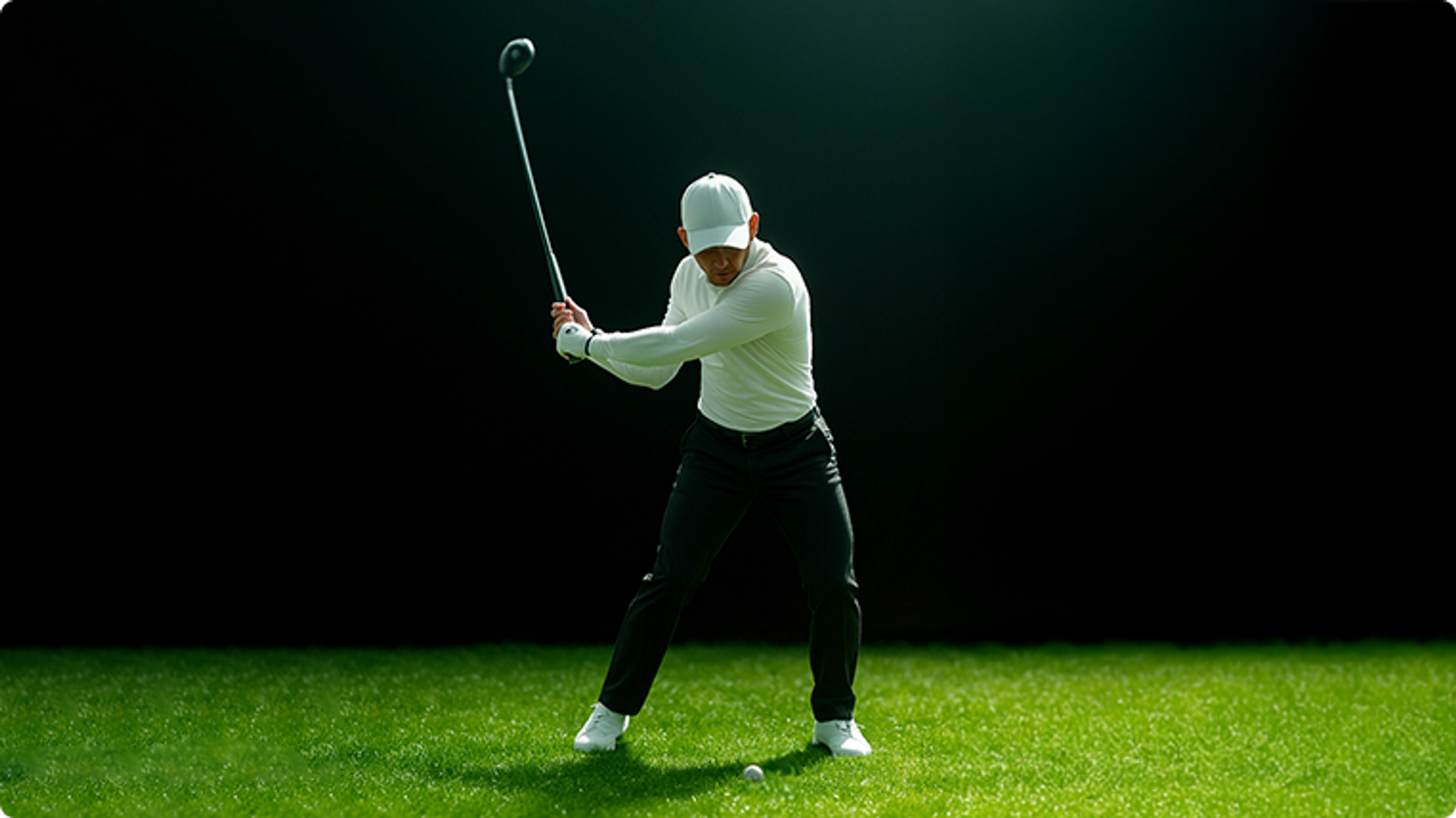 A golfer in a white shirt and cap swings a golf club on a green course with a golf ball on the grass, against a dark background.