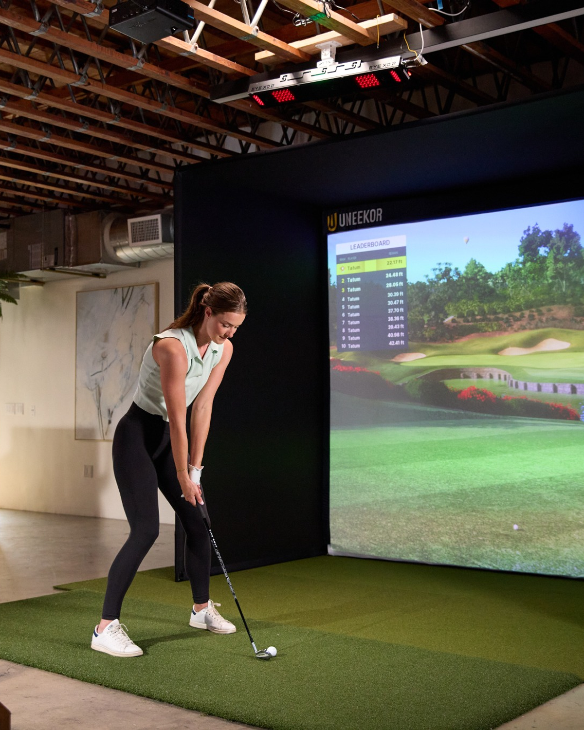 A woman plays golf on a simulator with a large screen displaying a golf course.