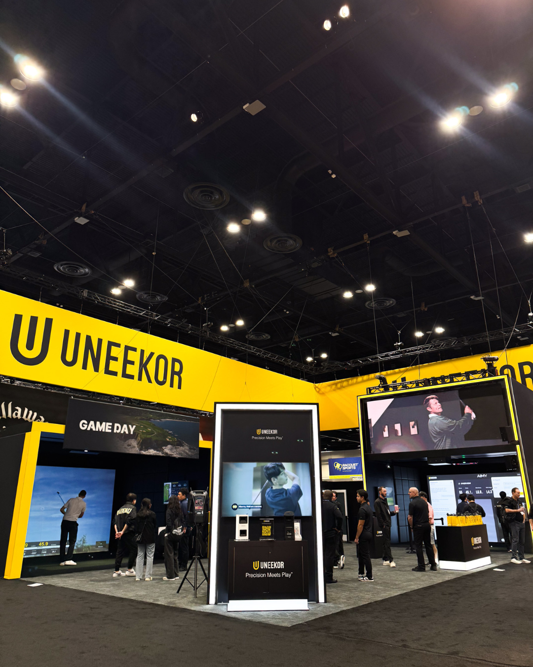 UNEKOR trade show booth featuring golf simulators, large video displays, and attendees.