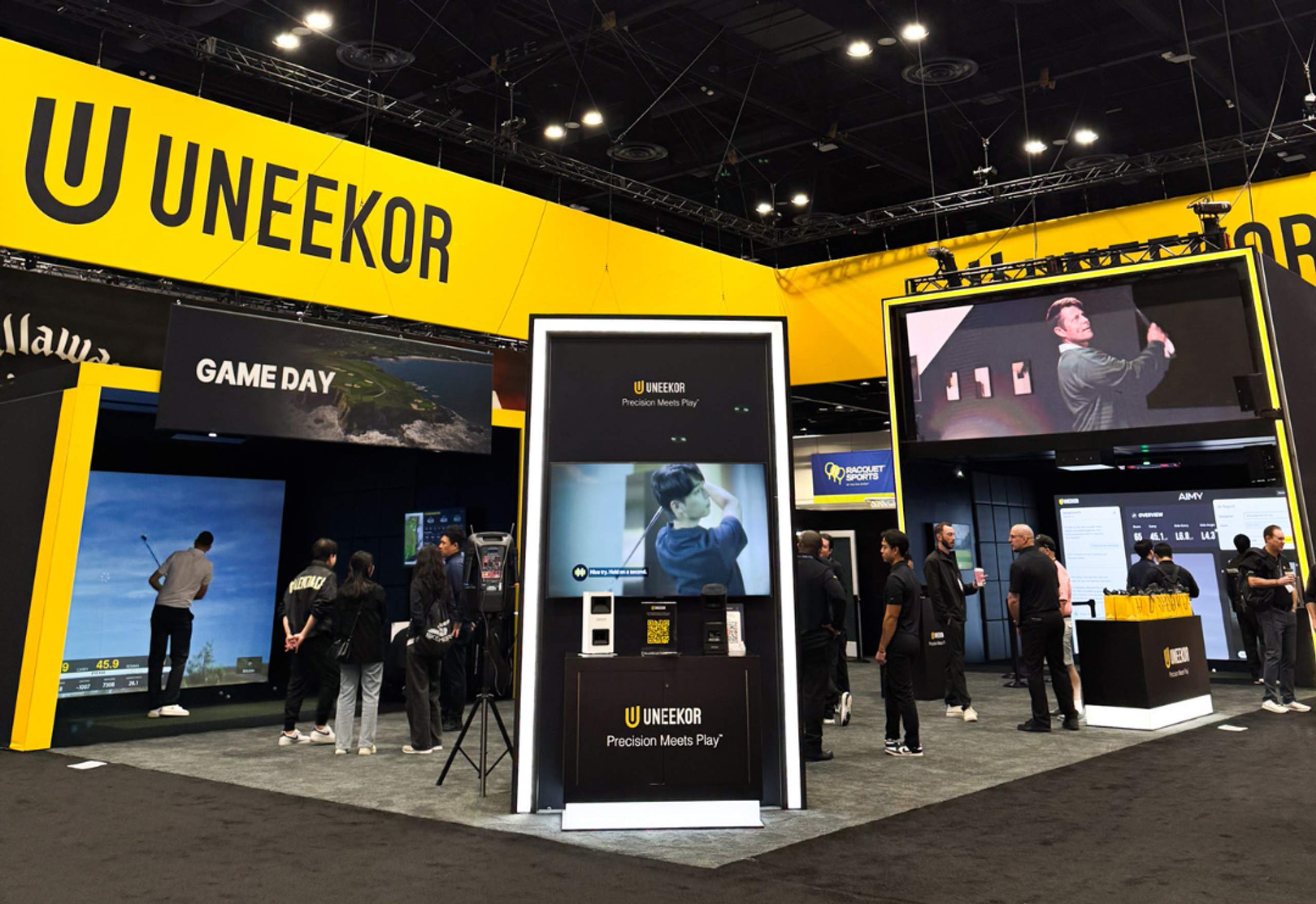 UNEKOR trade show booth featuring golf simulators, large video displays, and attendees.