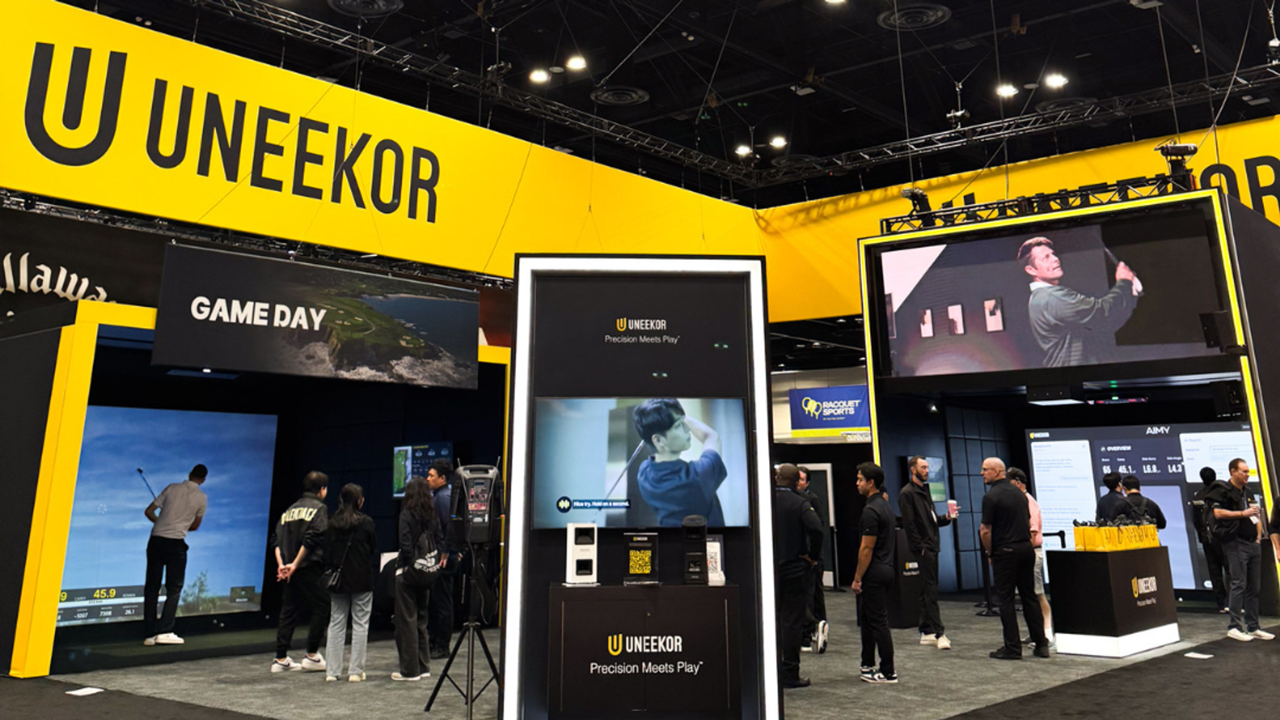 UNEKOR trade show booth featuring golf simulators, large video displays, and attendees.