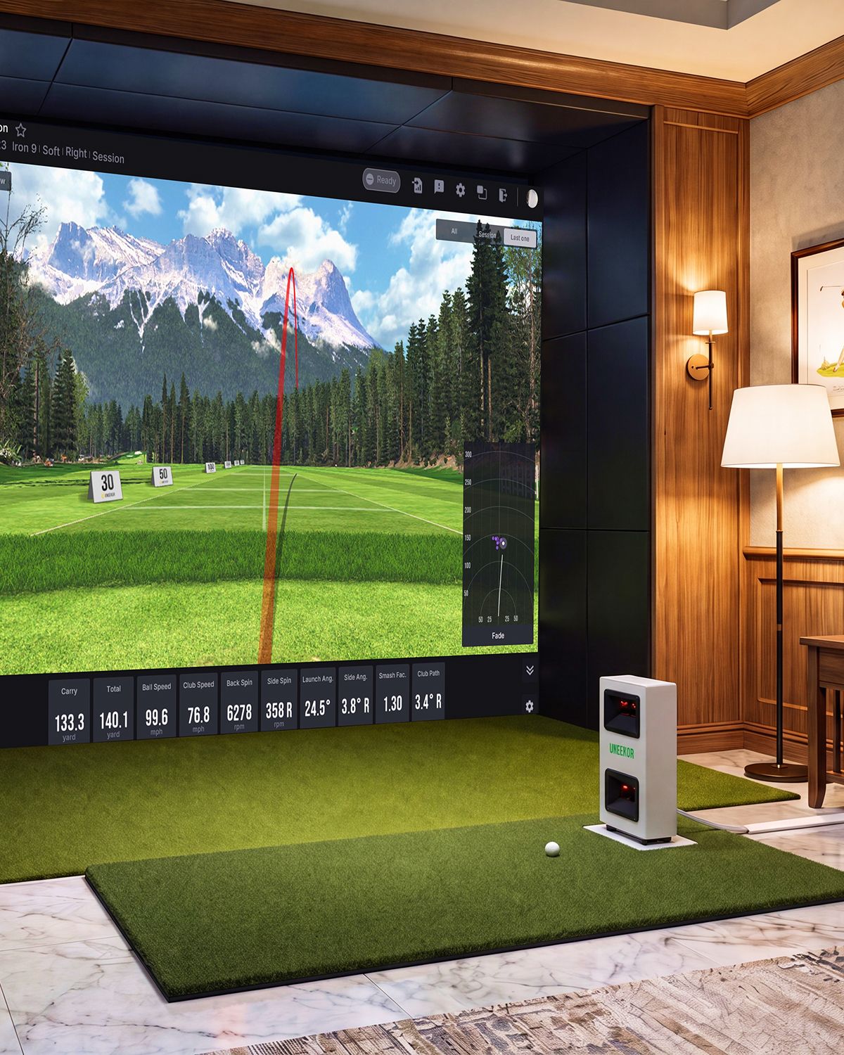 An indoor golf simulator setup with a large screen displaying a virtual golf course with mountains and a shot trajectory, a golf ball on a green mat, and a launch monitor.