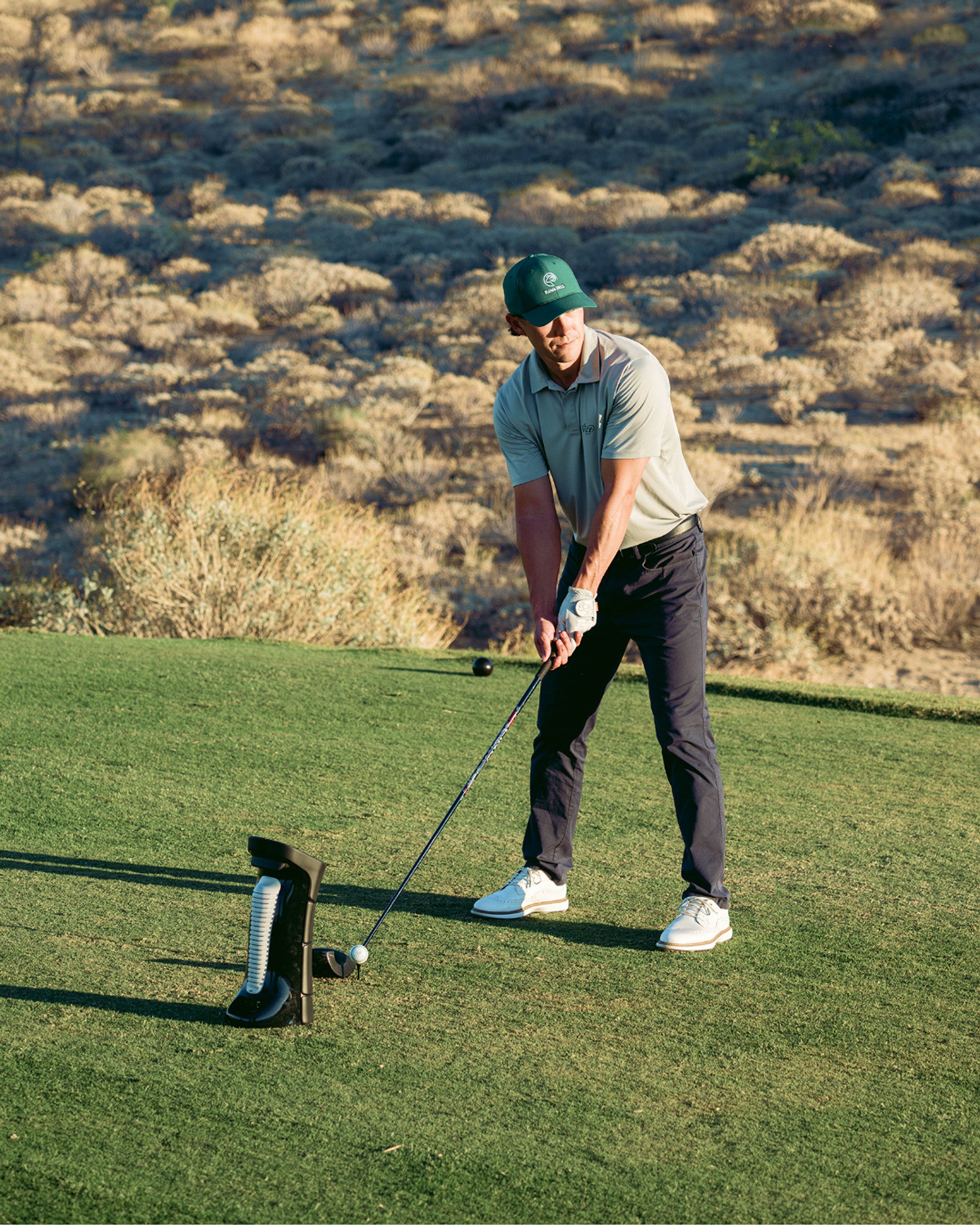 A man in a green cap and polo shirt prepares to hit a golf ball on a tee with a club.