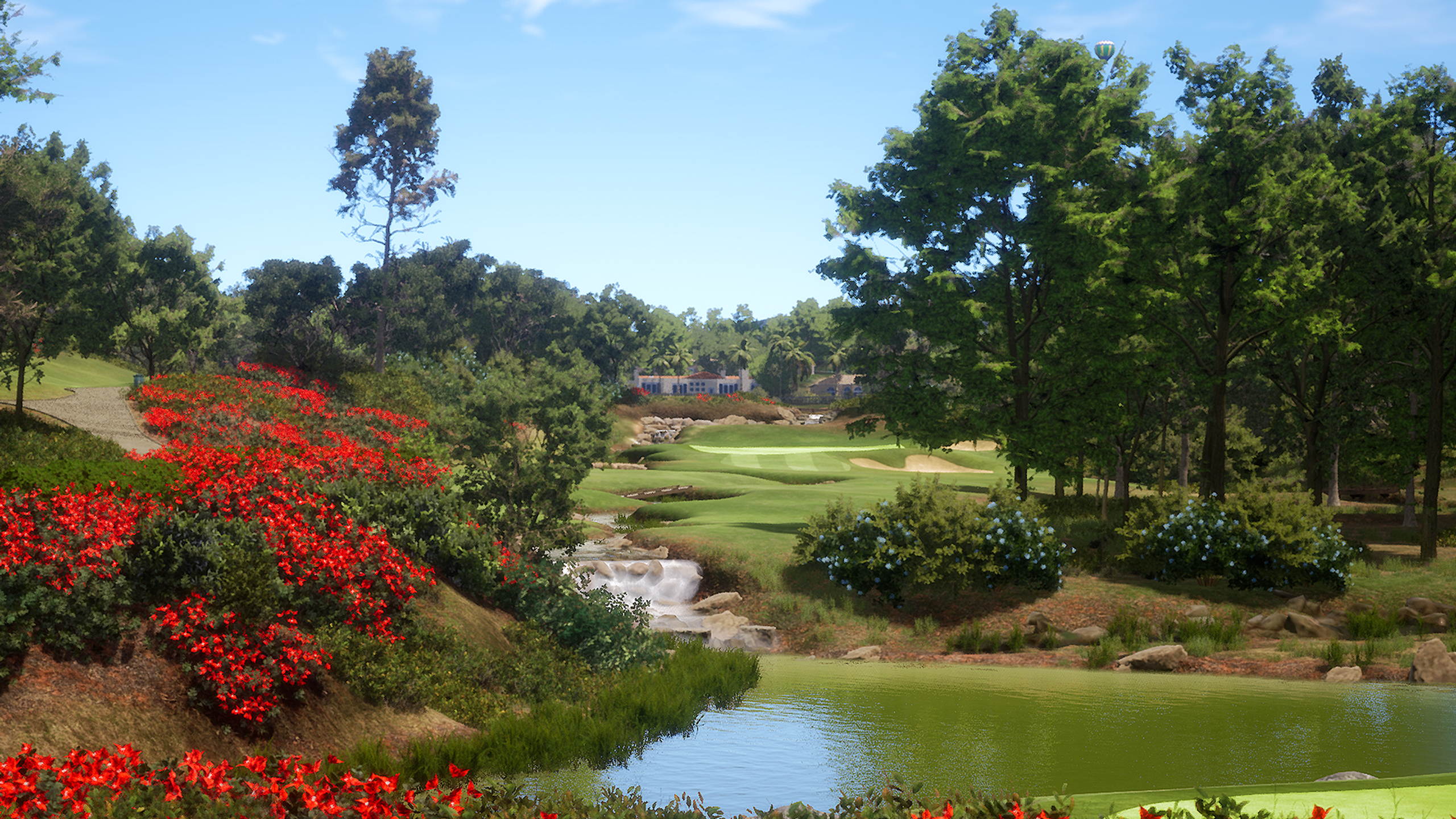A lush golf course with vibrant red flowers, a pond with a waterfall, and a hot air balloon under a blue sky.