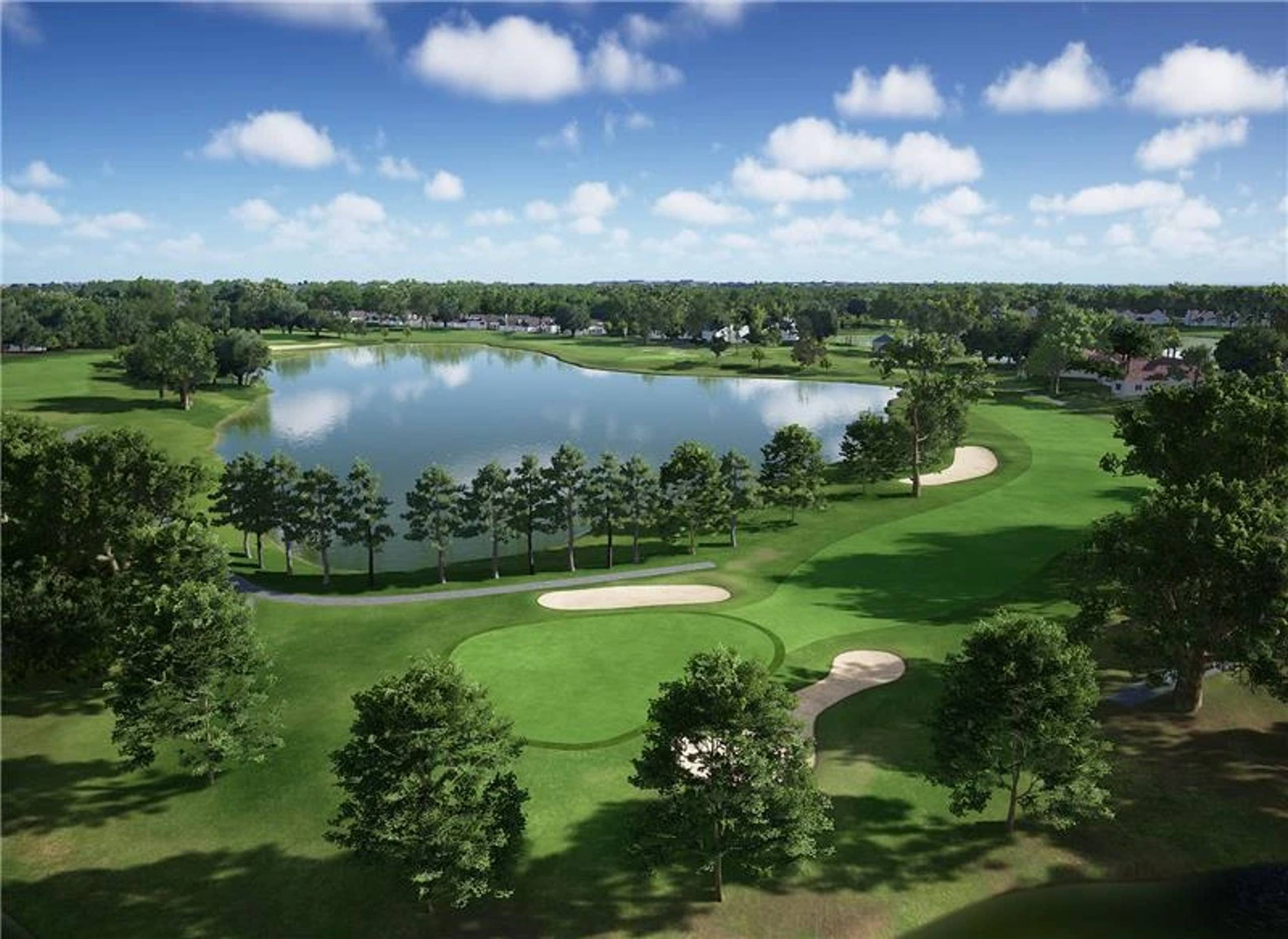 Aerial view of a golf course with a large lake, greens, sand bunkers, and trees under a blue sky.