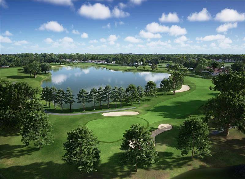 Aerial view of a golf course with a large lake, greens, sand bunkers, and trees under a blue sky.