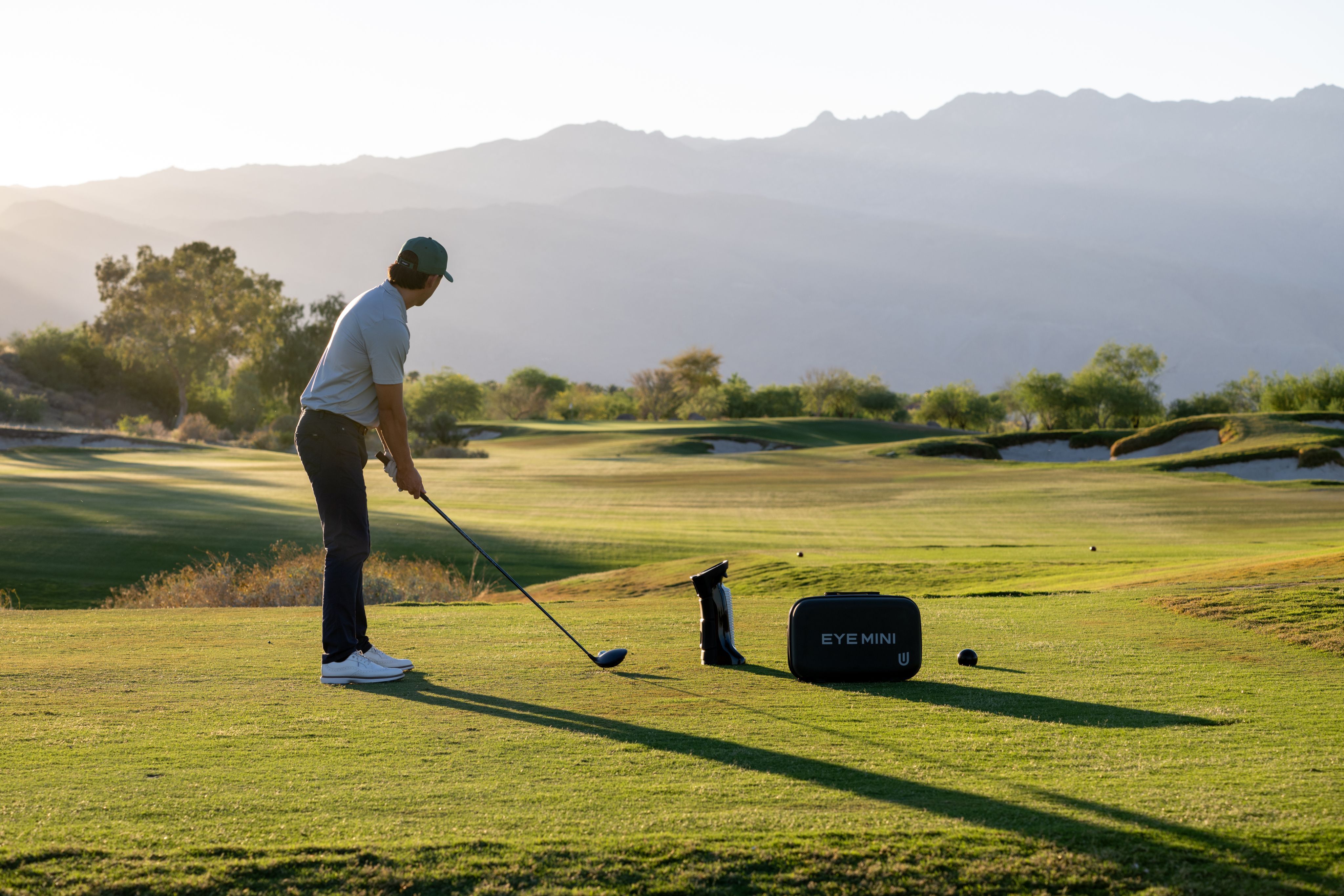 Golfer on a course with an EYE MINI device and mountains in the background.