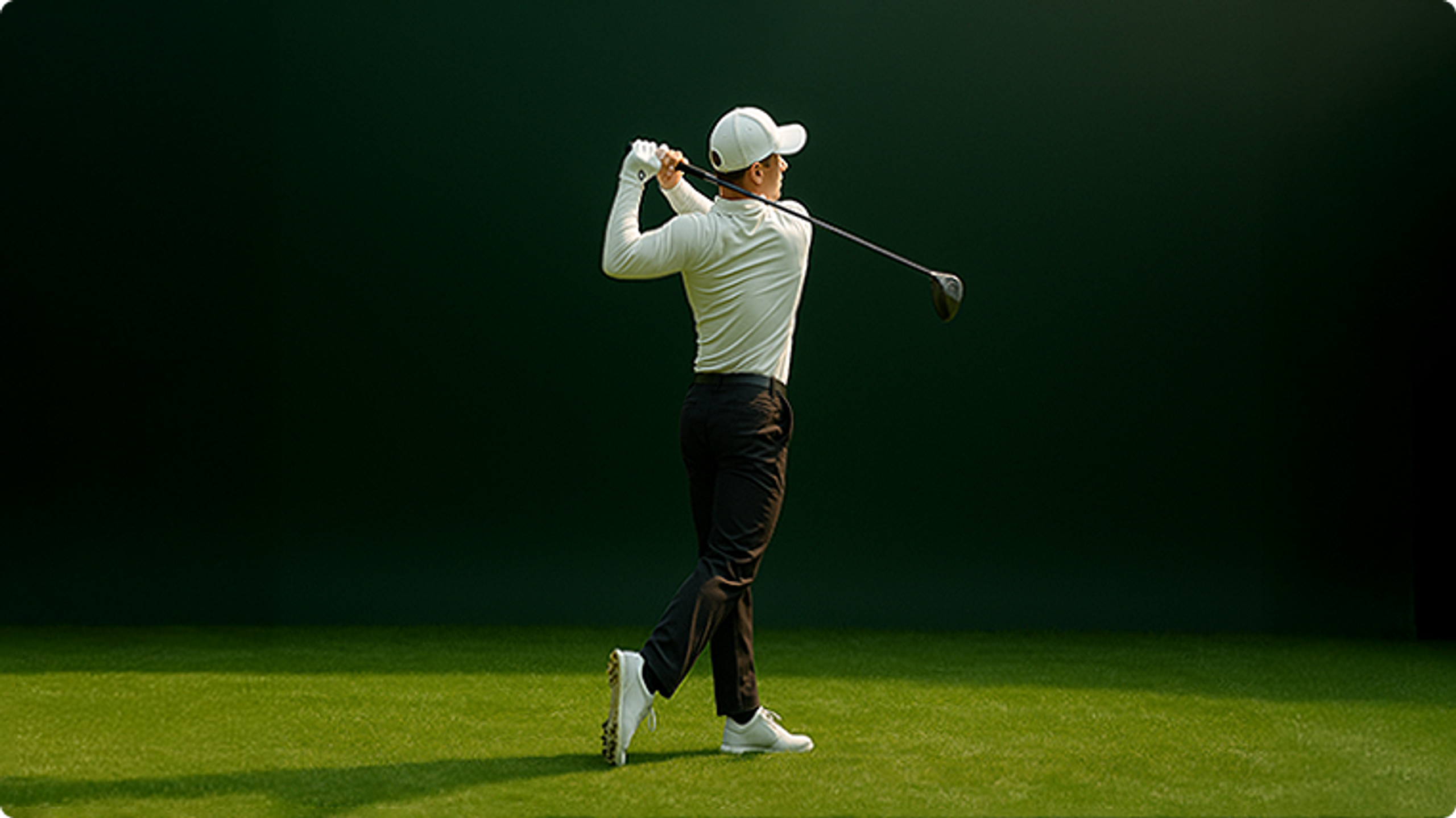 Rear view of a golfer in a white cap and light shirt swinging a driver on a green course.