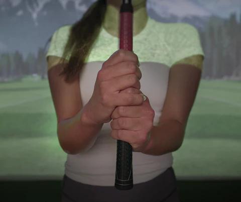 Eine Person hält in einem Golfsimulator einen Golfschläger mit beiden Händen.
