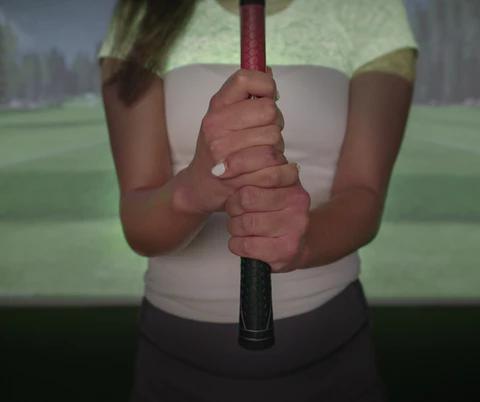 Die Hände einer Person, die einen Golfschläger hält, mit einem Golfplatzsimulator im Hintergrund.
