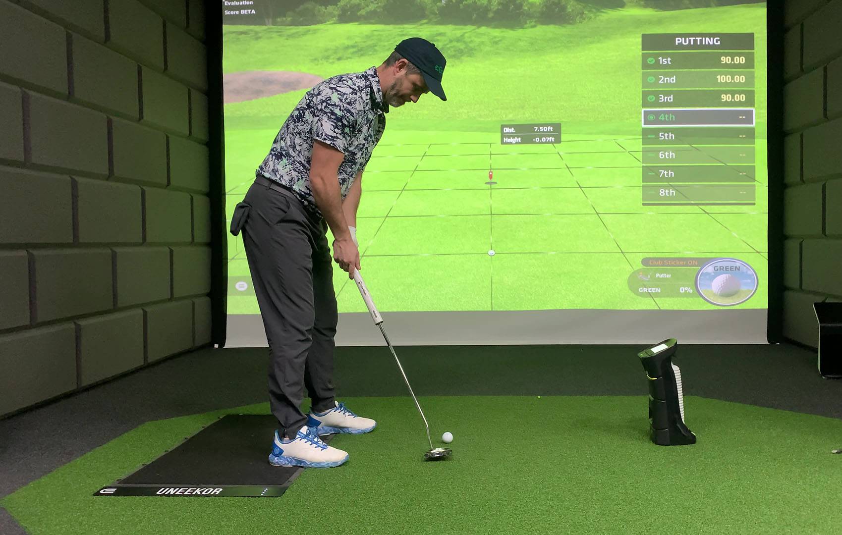 A man putting a golf ball in a golf simulator with a virtual green projected on a large screen.