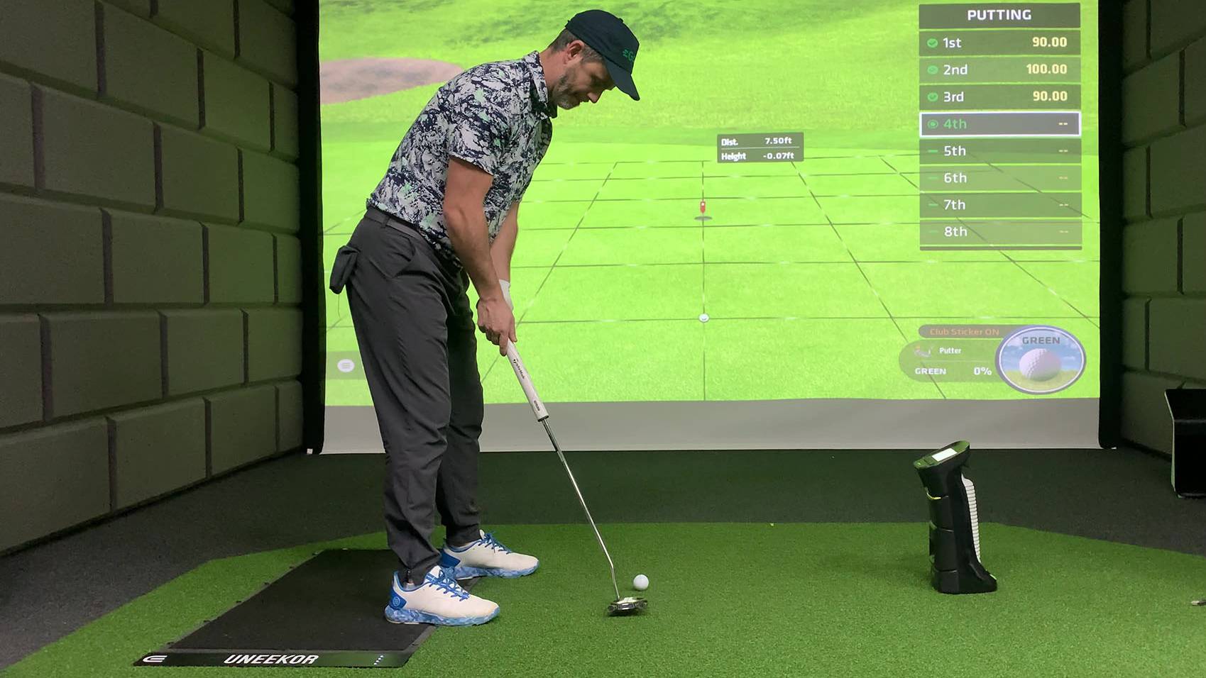 A man putting a golf ball in a golf simulator with a virtual green projected on a large screen.
