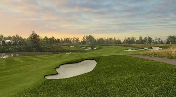 Golf course with green fairways, sand bunkers, a pond, and trees at sunset.