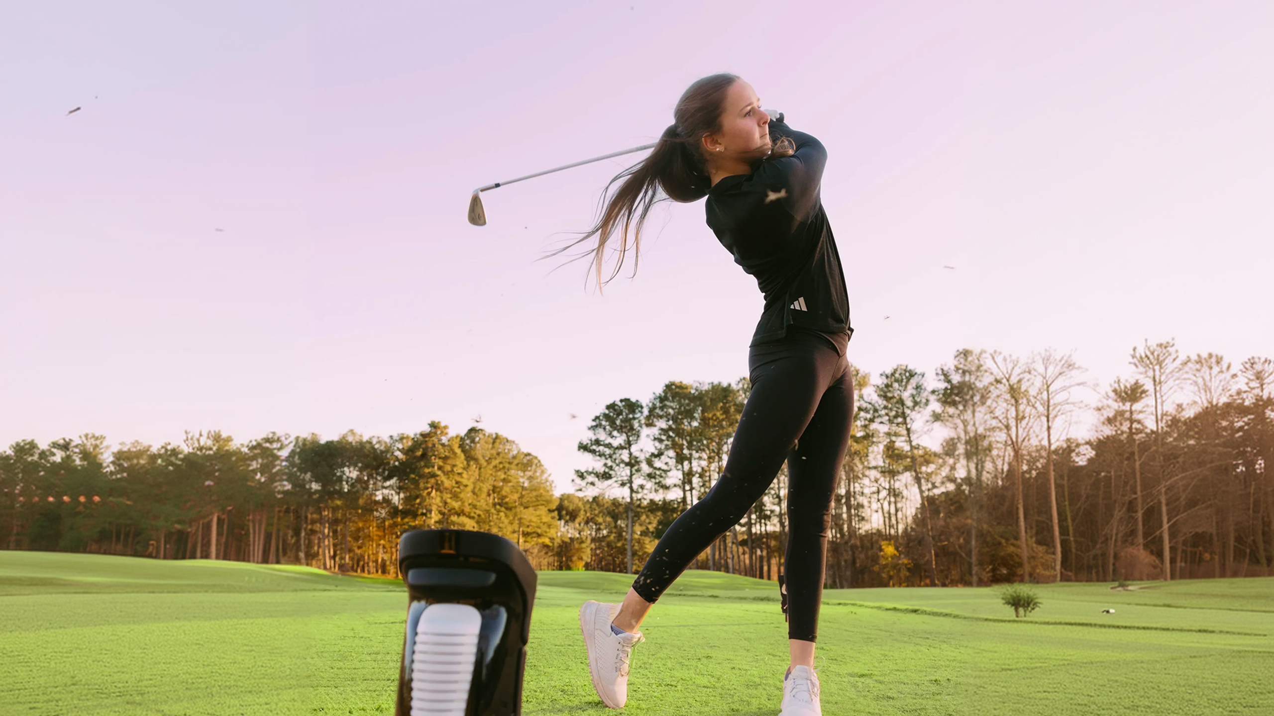 A woman in black athletic wear swings a golf club on a golf course.