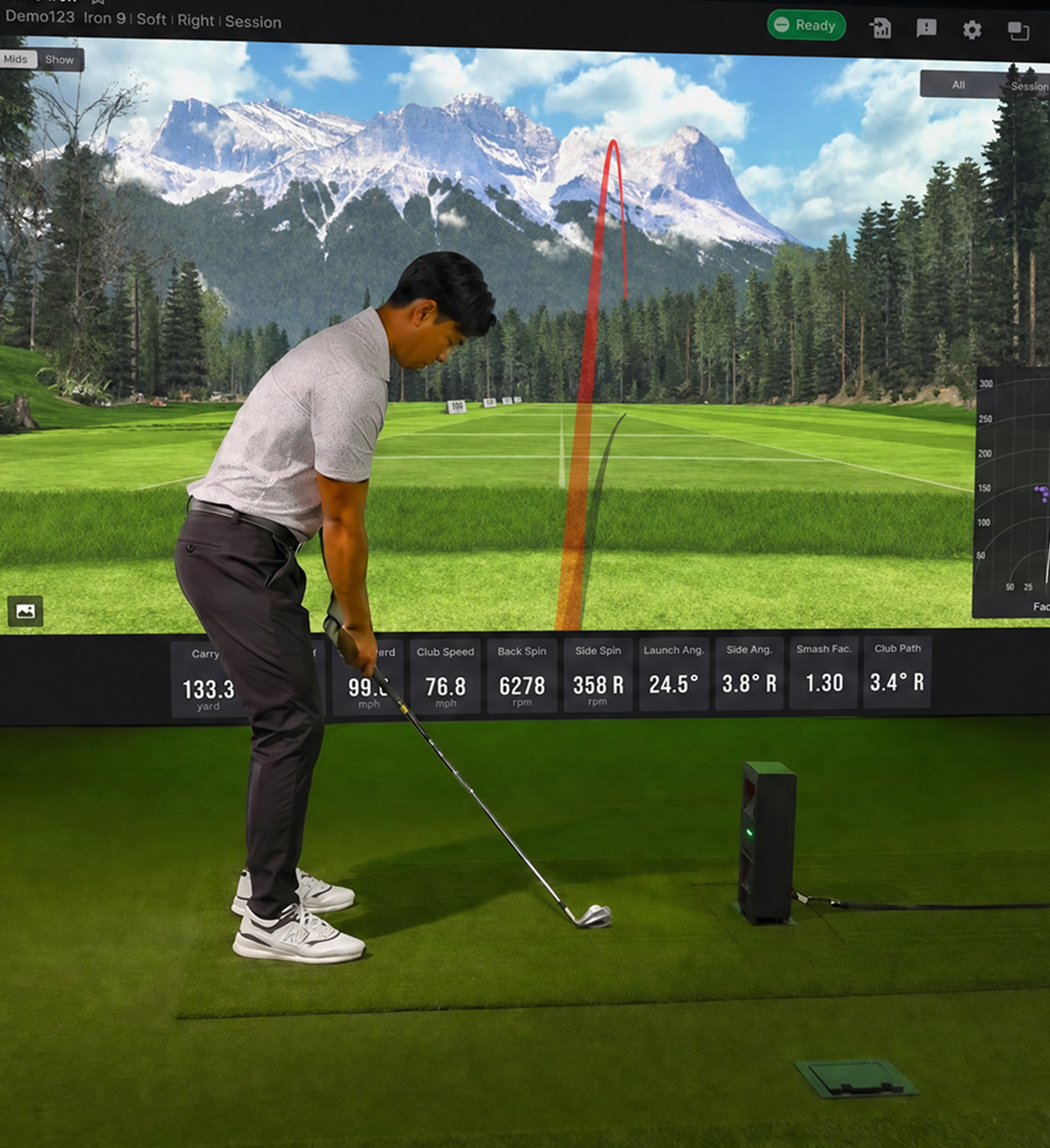 A man prepares to hit a golf ball in a golf simulator, with a launch monitor and a large screen displaying a virtual course.