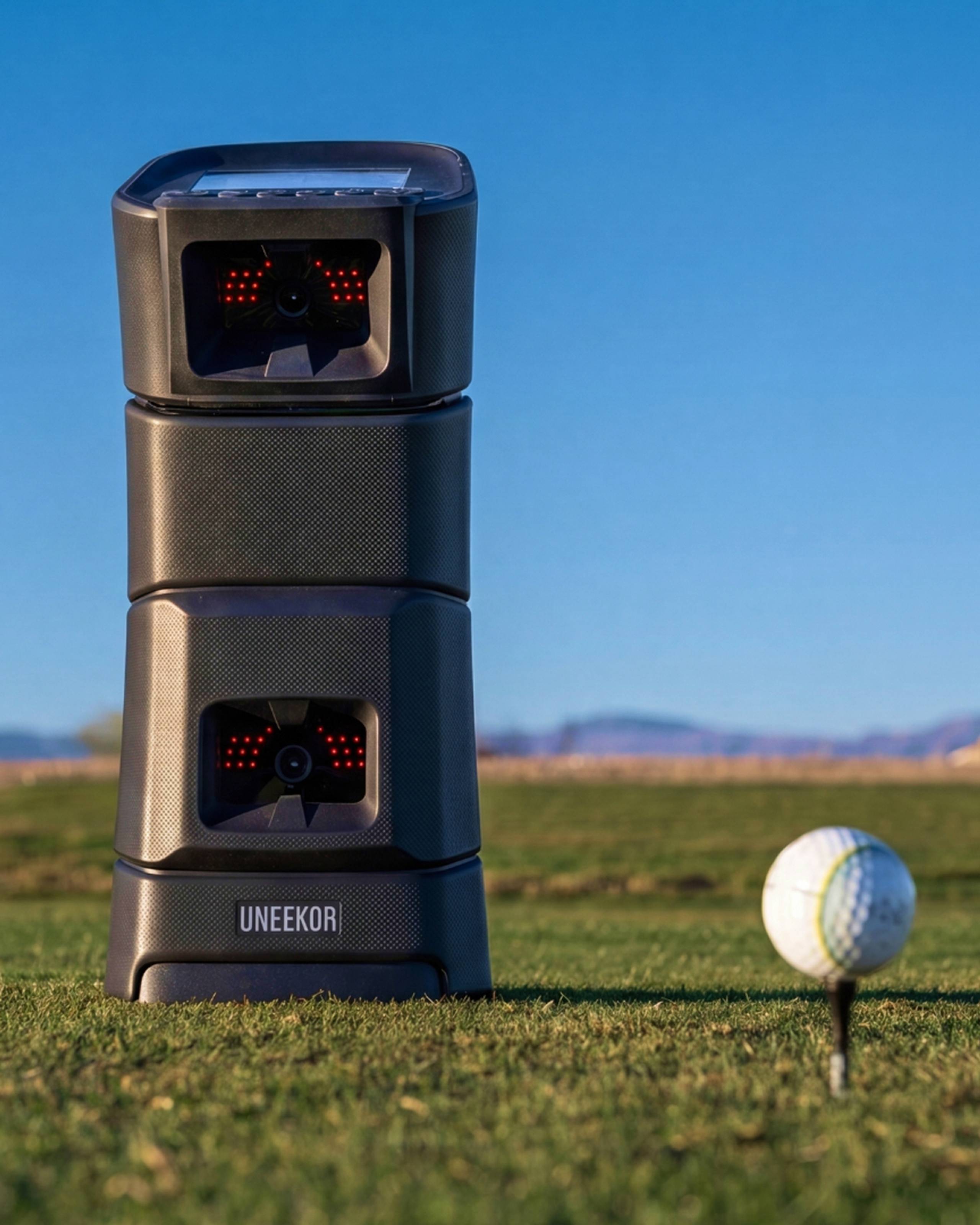 A Uneekor golf launch monitor on a course next to a golf ball on a tee.