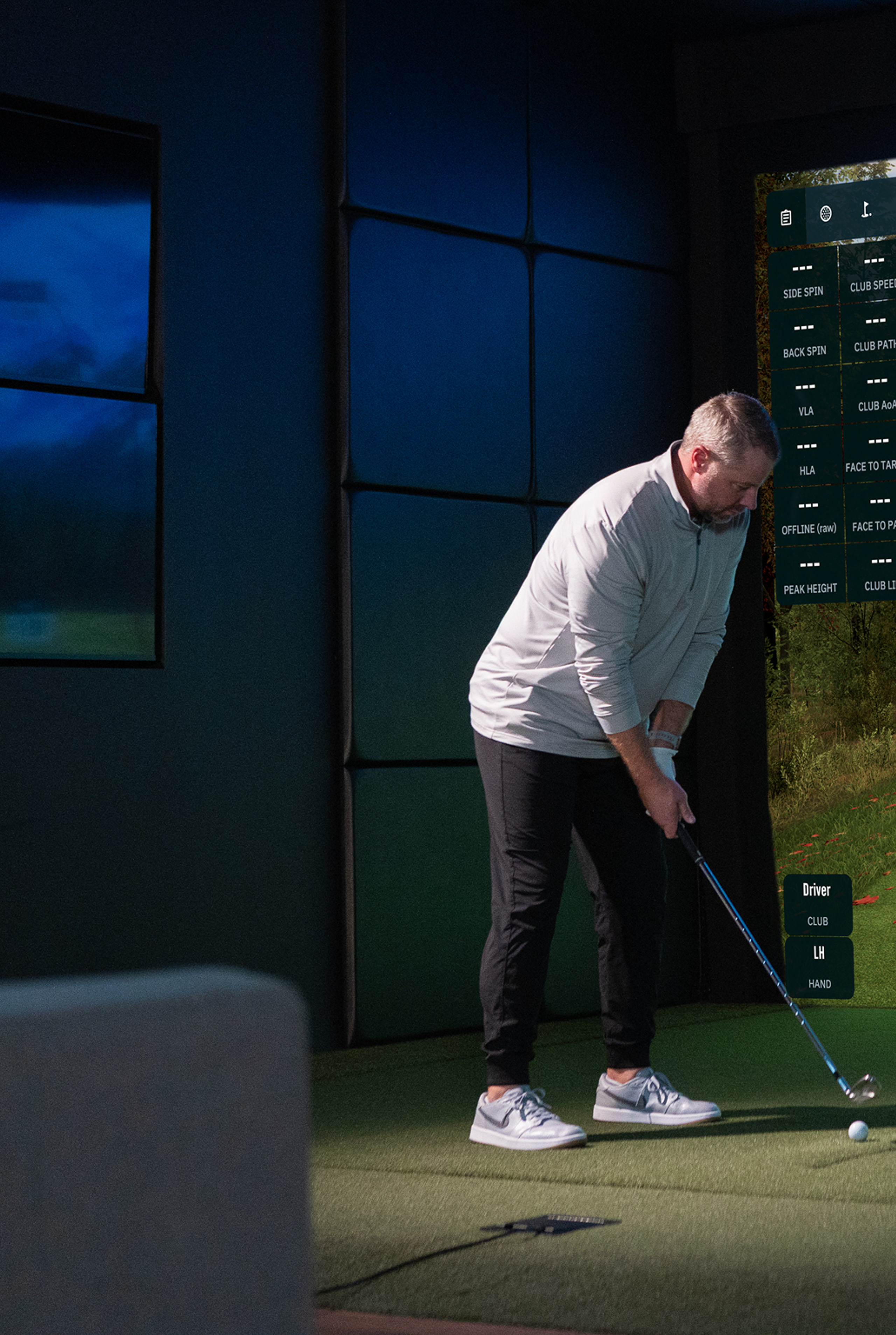A man playing golf on an indoor simulator showing a virtual course.