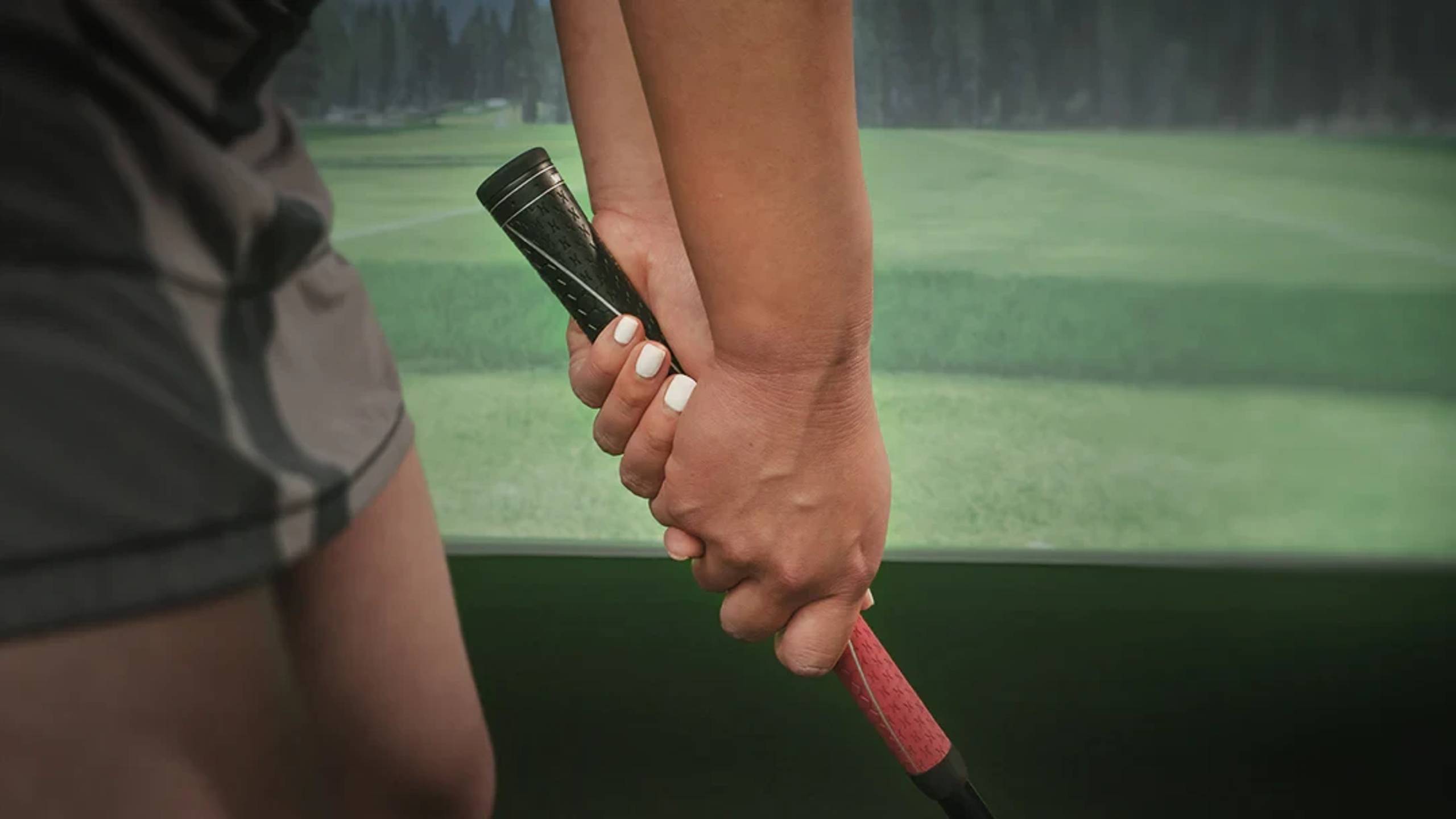 Close-up of hands gripping a golf club in a golf simulator.