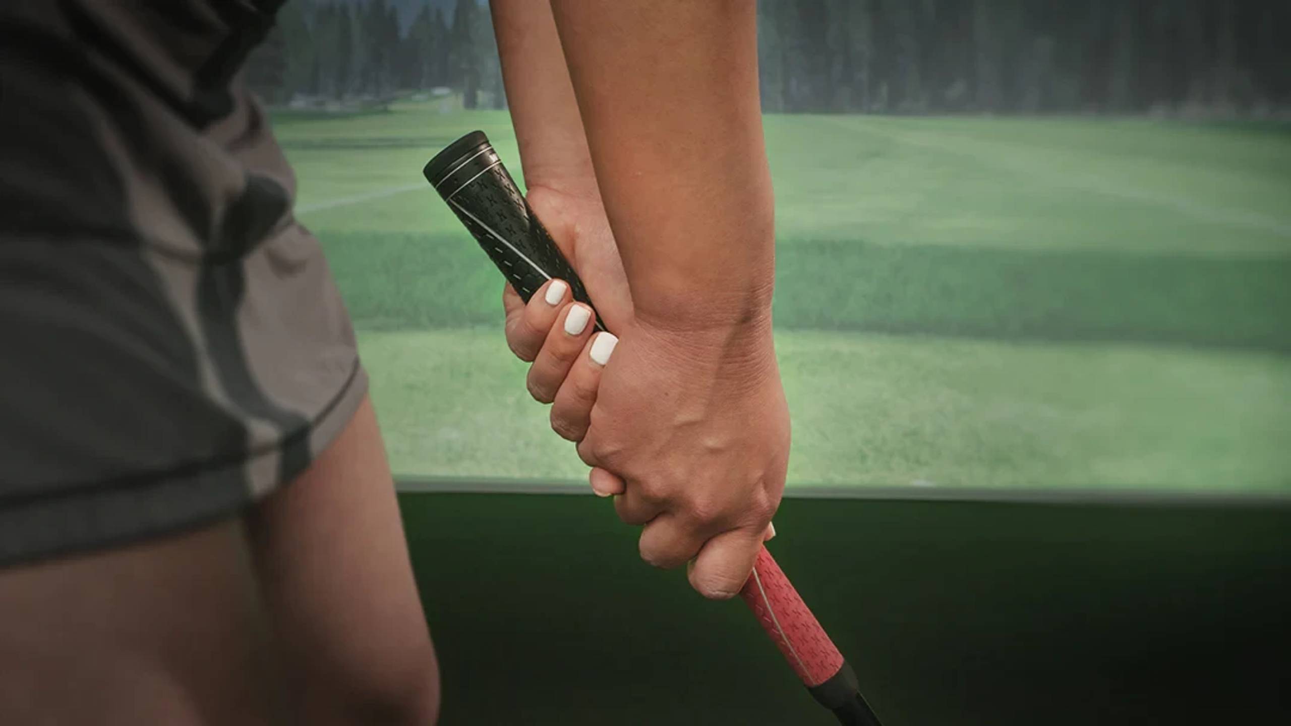Close-up of hands gripping a golf club in a golf simulator.