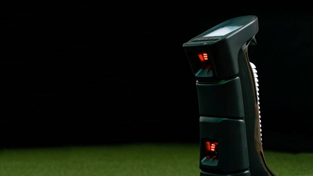 A dark UNIEQR golf launch monitor with red lights and a screen sits on green turf.