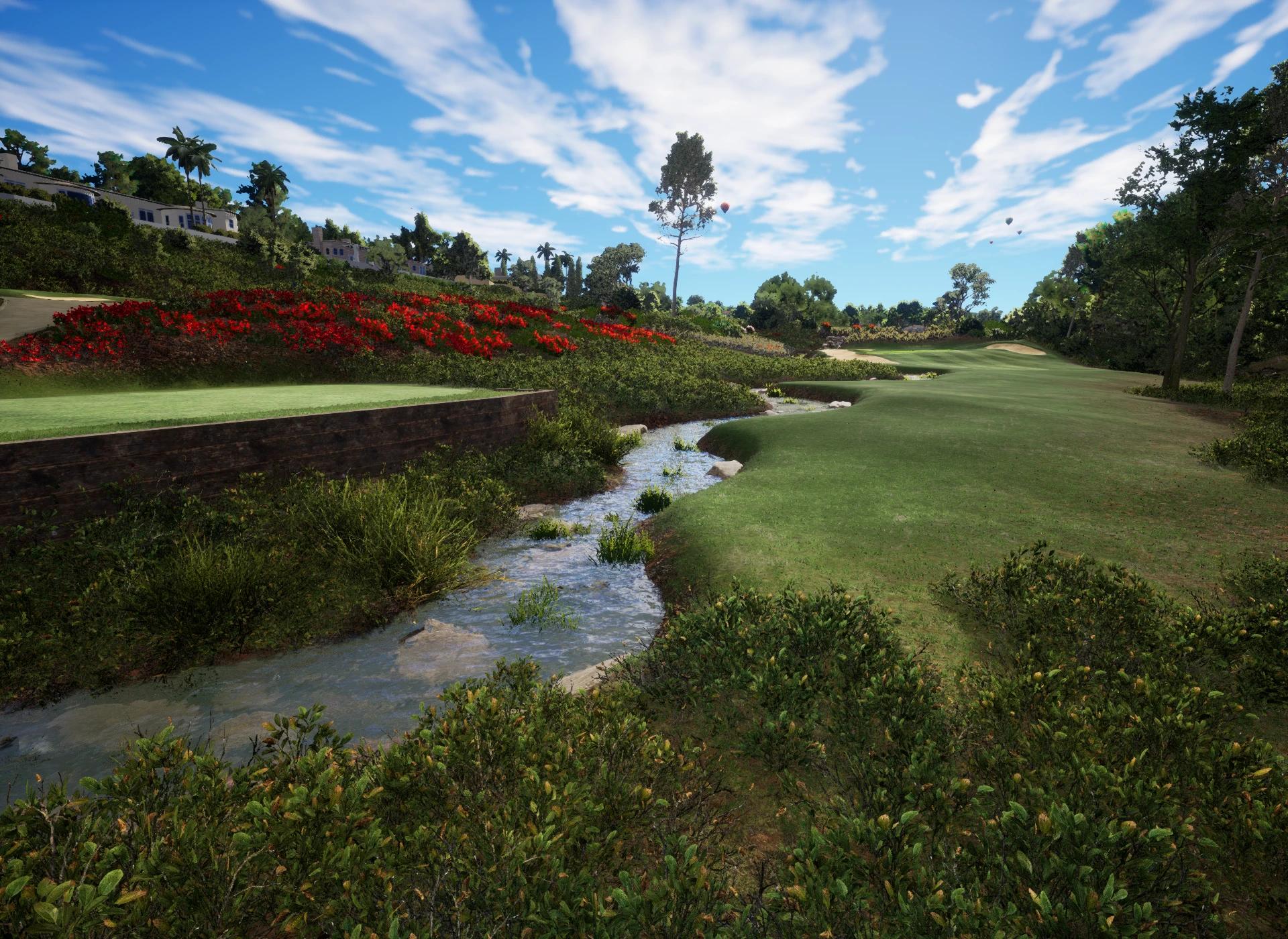 A scenic golf course with a winding stream, a hillside covered in red flowers, distant houses, and a green fairway under a blue sky.