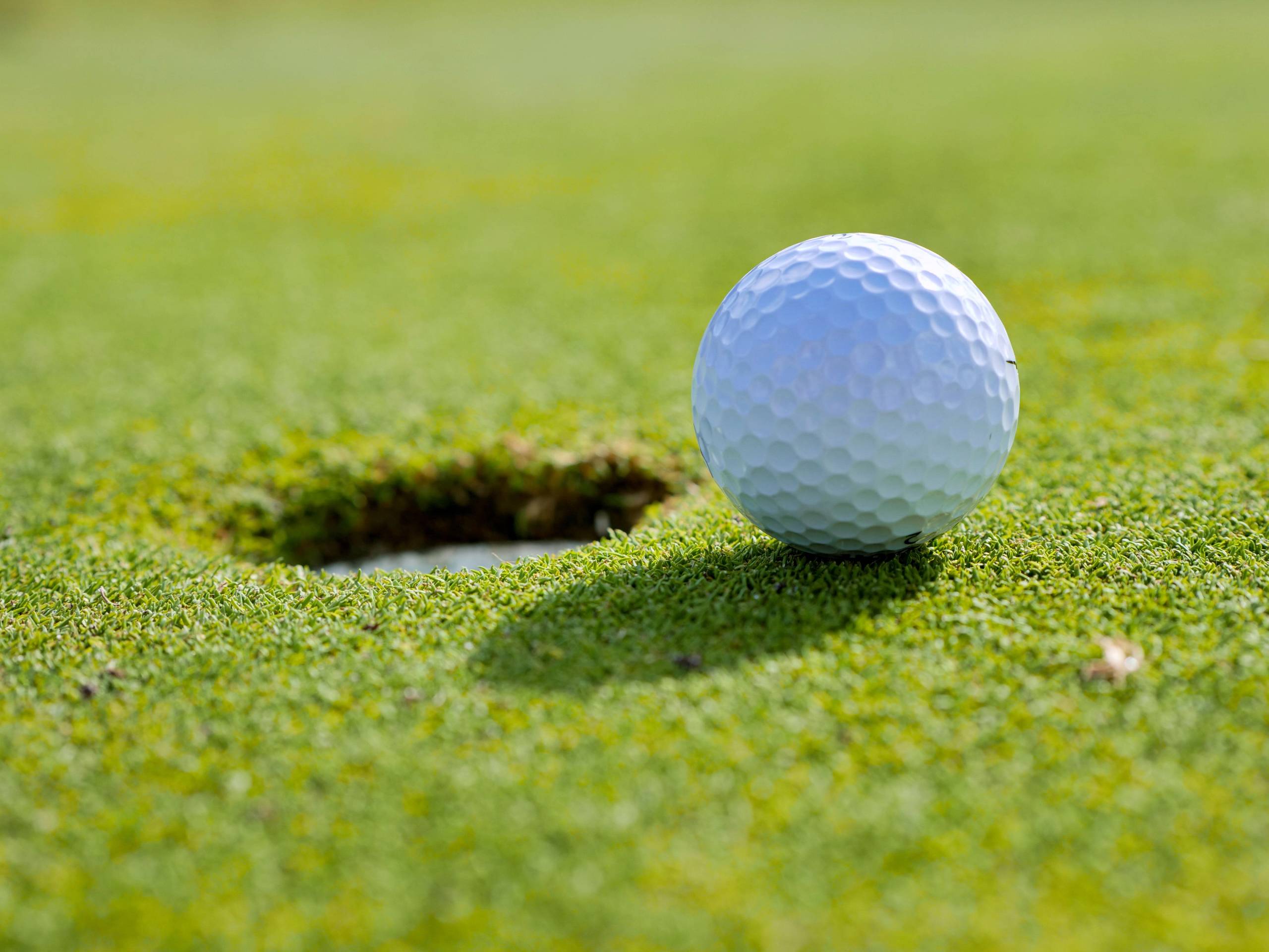 A white golf ball rests next to the hole on a green putting surface.
