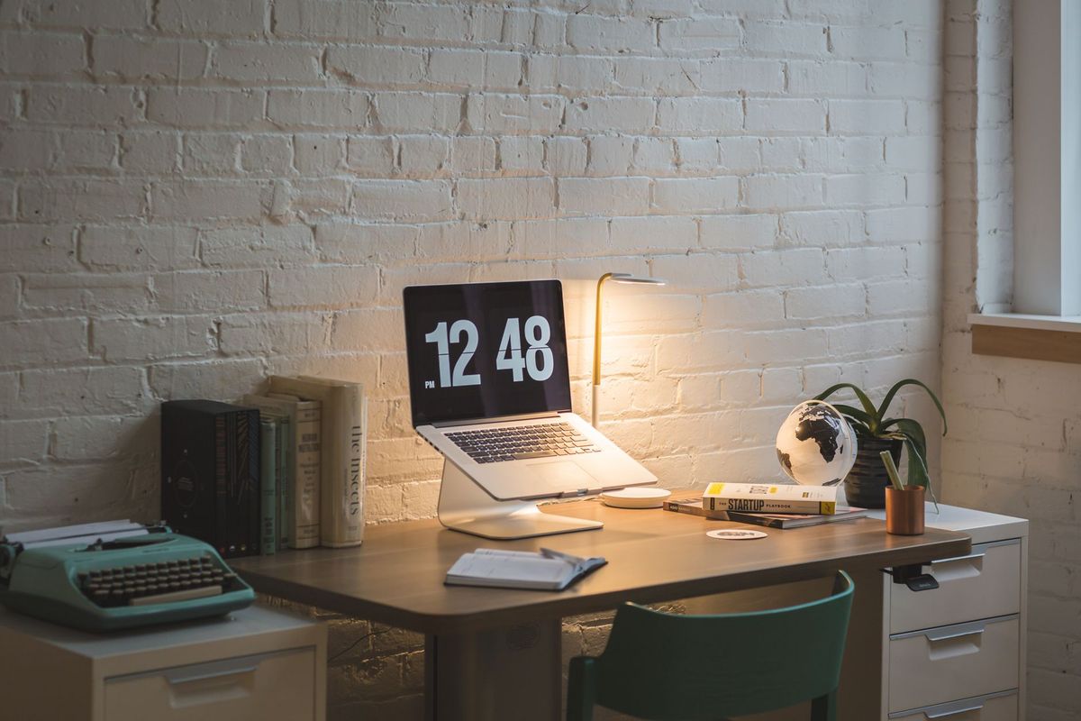 A well-organized workspace featuring a laptop, books, and a lamp on a wooden desk.