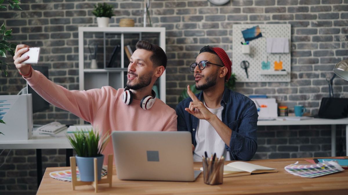 Two young men taking a selfie in a modern office setting, surrounded by creative tools and decor.