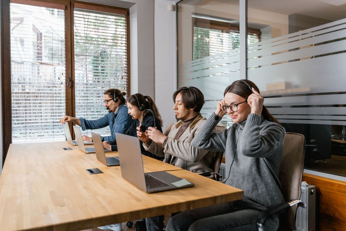Professional team in a modern office setting using laptops and headsets for communication.