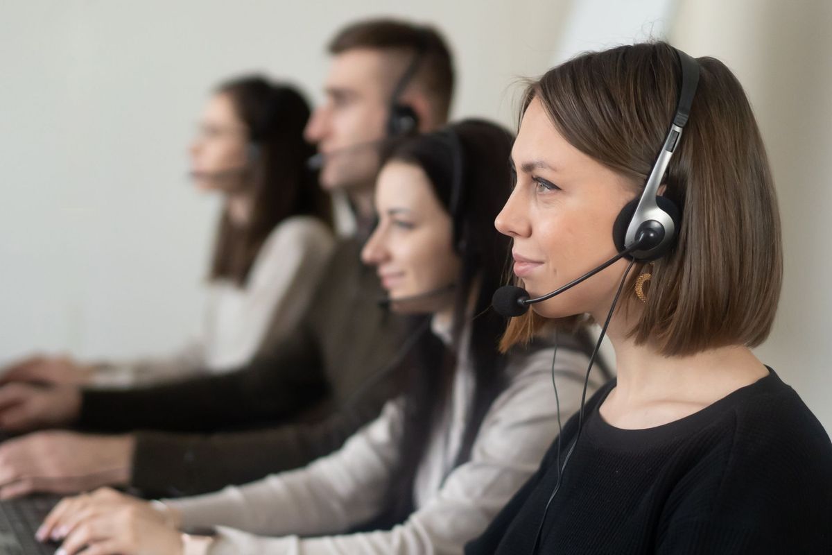 Side view of young coworkers in casual clothes sitting in light workplace with headphones with microphone while surfing