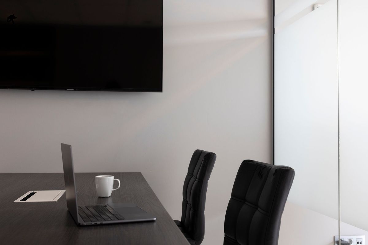 A sleek, modern office setup with a laptop, cup, and TV in an empty conference room.