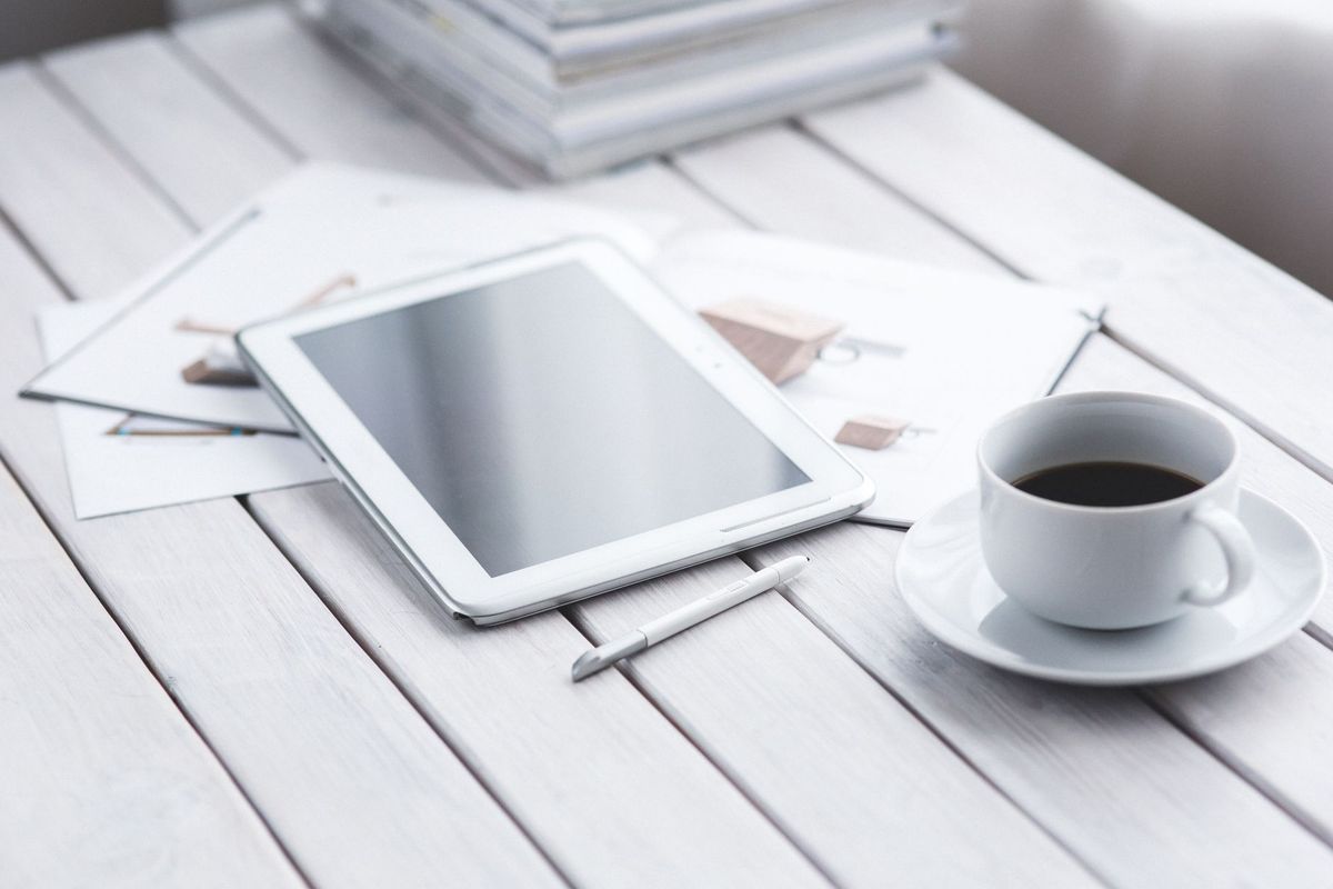 White tablet with stylus and coffee cup on modern office desk setup.