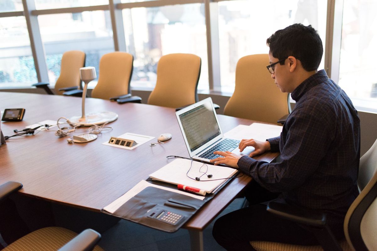 A professional adult sitting at a desk with a laptop in a bright, modern conference room.