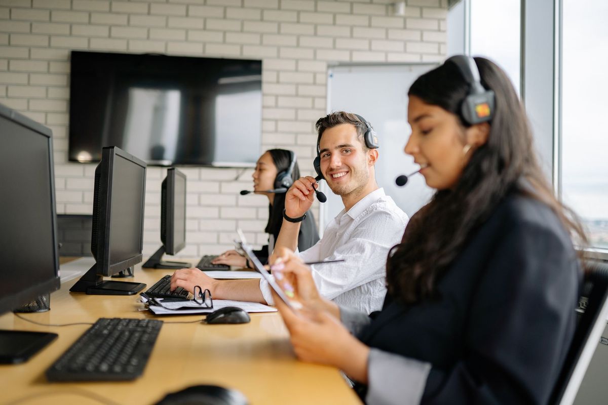 Smiling call center agents wearing headsets, working together in a modern office setting.