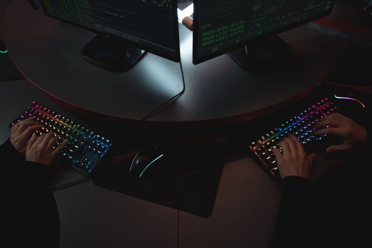 Two people typing on RGB keyboards with code on screens, indicating a cybersecurity environment.