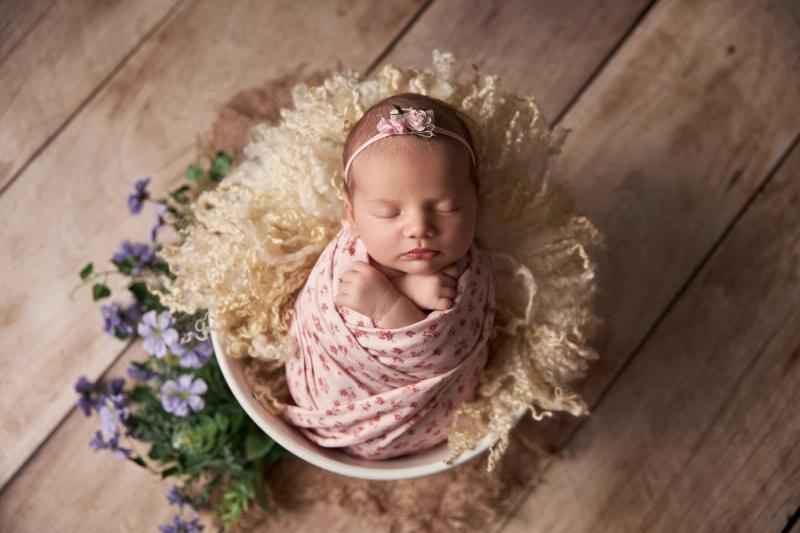 Miminko holčička v bílém kyblíku s růžovým květinovým wrapem a květinami.
