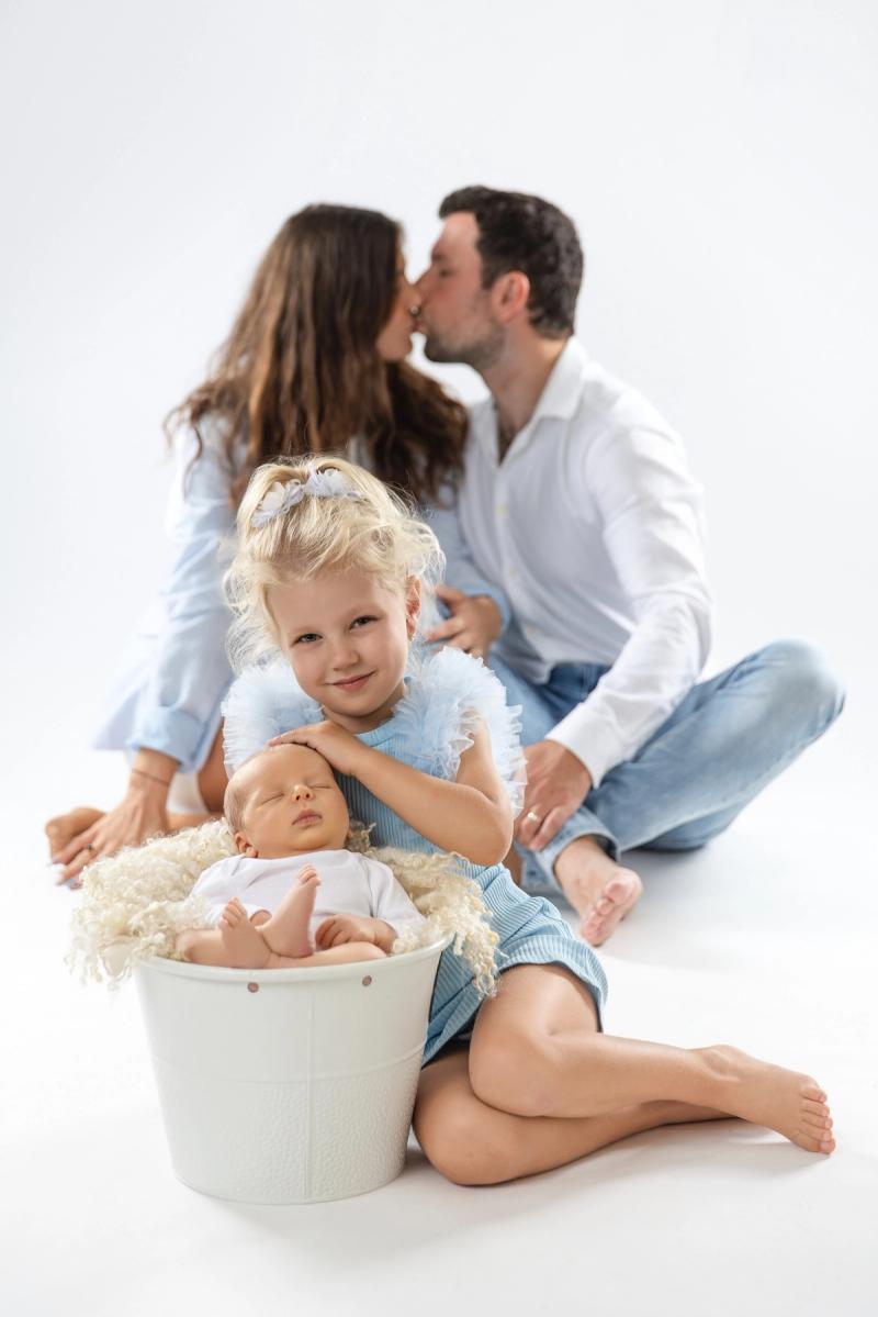 Rodinná fotografie, rodiče se líbají u Newborn miminka v košíku.