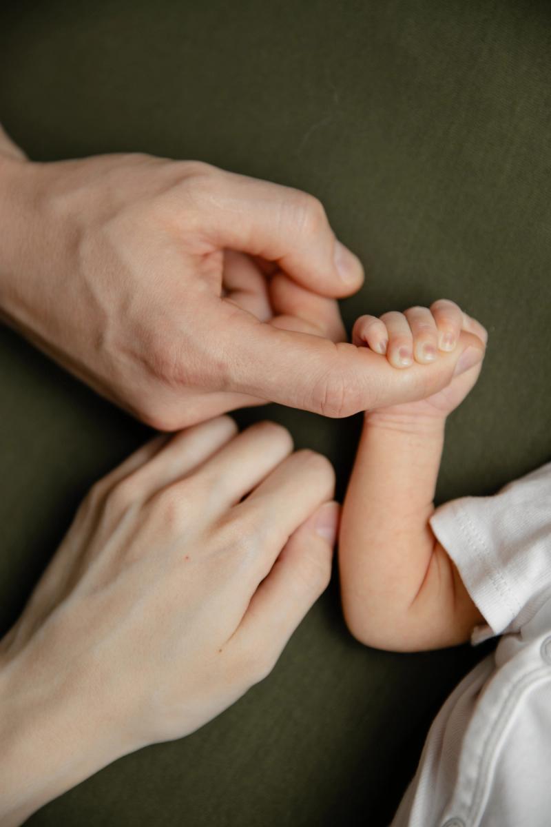 Detail ručičky novorozence držící prst rodiče na zeleném pozadí.
