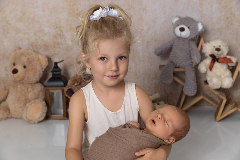 Sourozenecké foto holčičky, která má v náruči miminko s plyšáky.