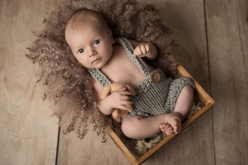 Miminko v košíku v šedých lacláčích na dřevěné podlaze.